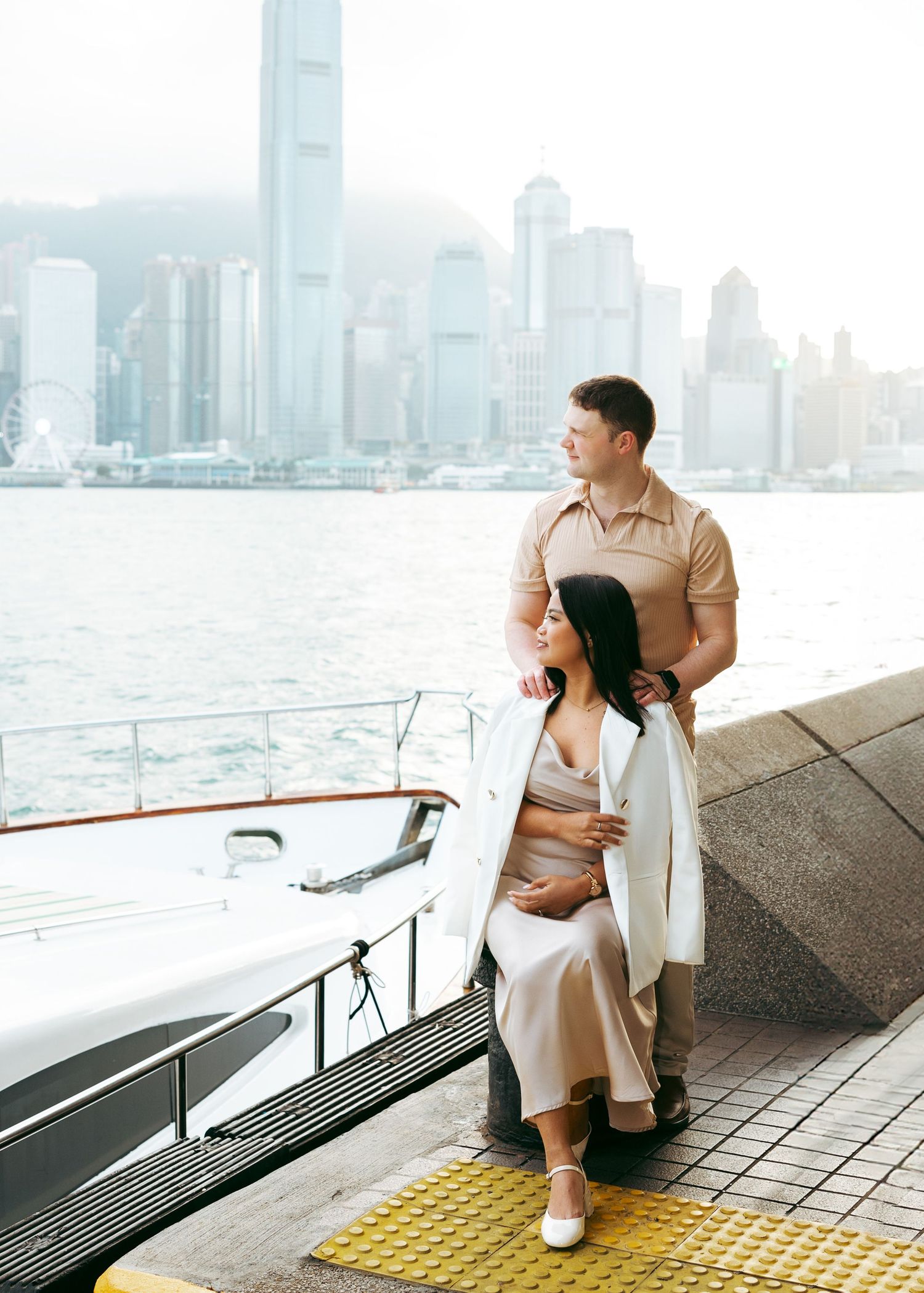 Couple sit along the harbor promenade overlooking Hong Kong's iconic skyline across Victoria Harbour. Couple Session in Hong Kong