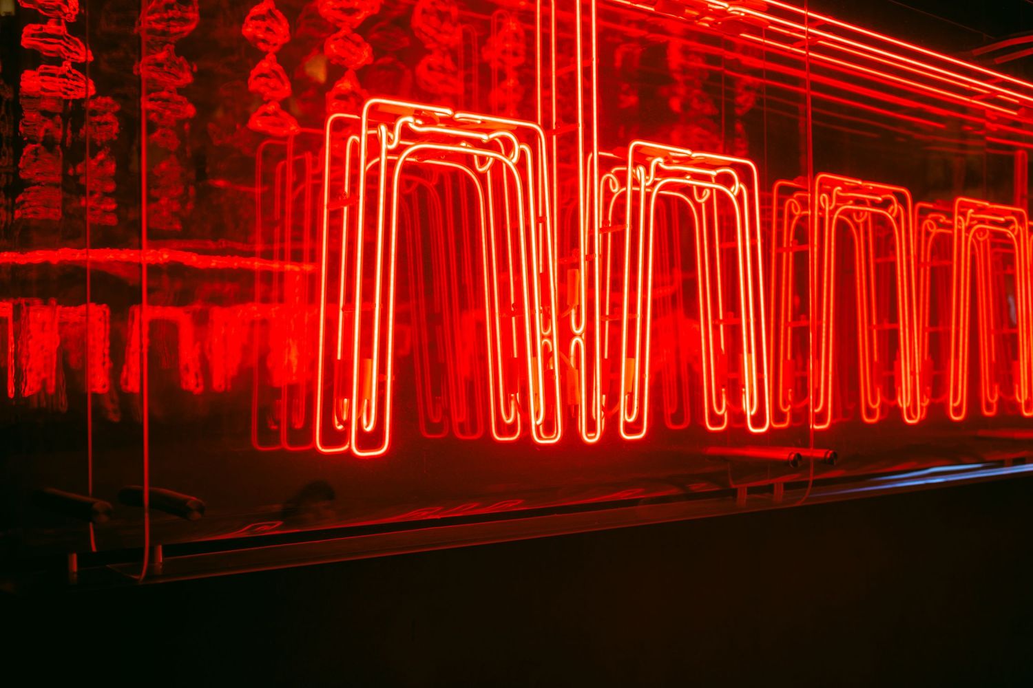 Vibrant red neon lights in zigzag arch patterns glowing against a dark background create a geometric illuminated display. Taikwun, Hong Kong