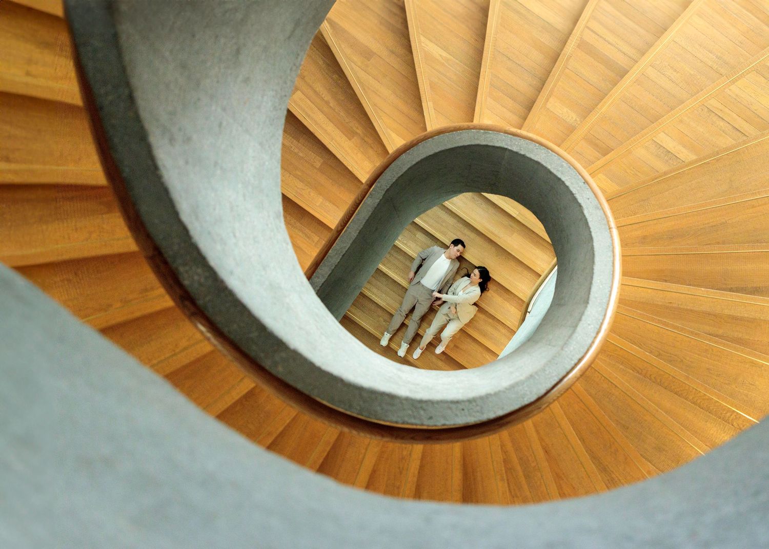 A modern spiral wooden staircase circles down with natural light illuminating. Couple Photoshoot in Hong Kong