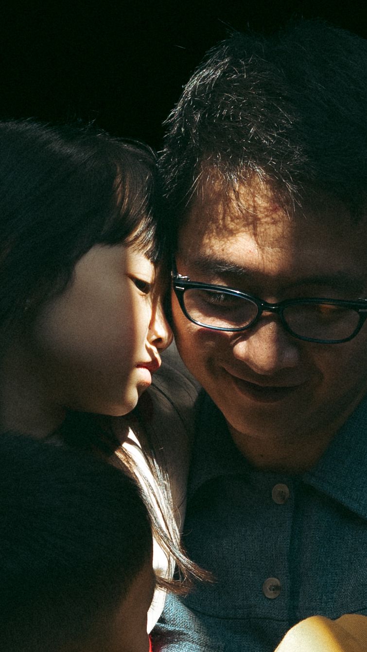 Intimate moment captured in dramatic lighting as daughter and father in glasses share a close interaction. family photographer in Hong Kong