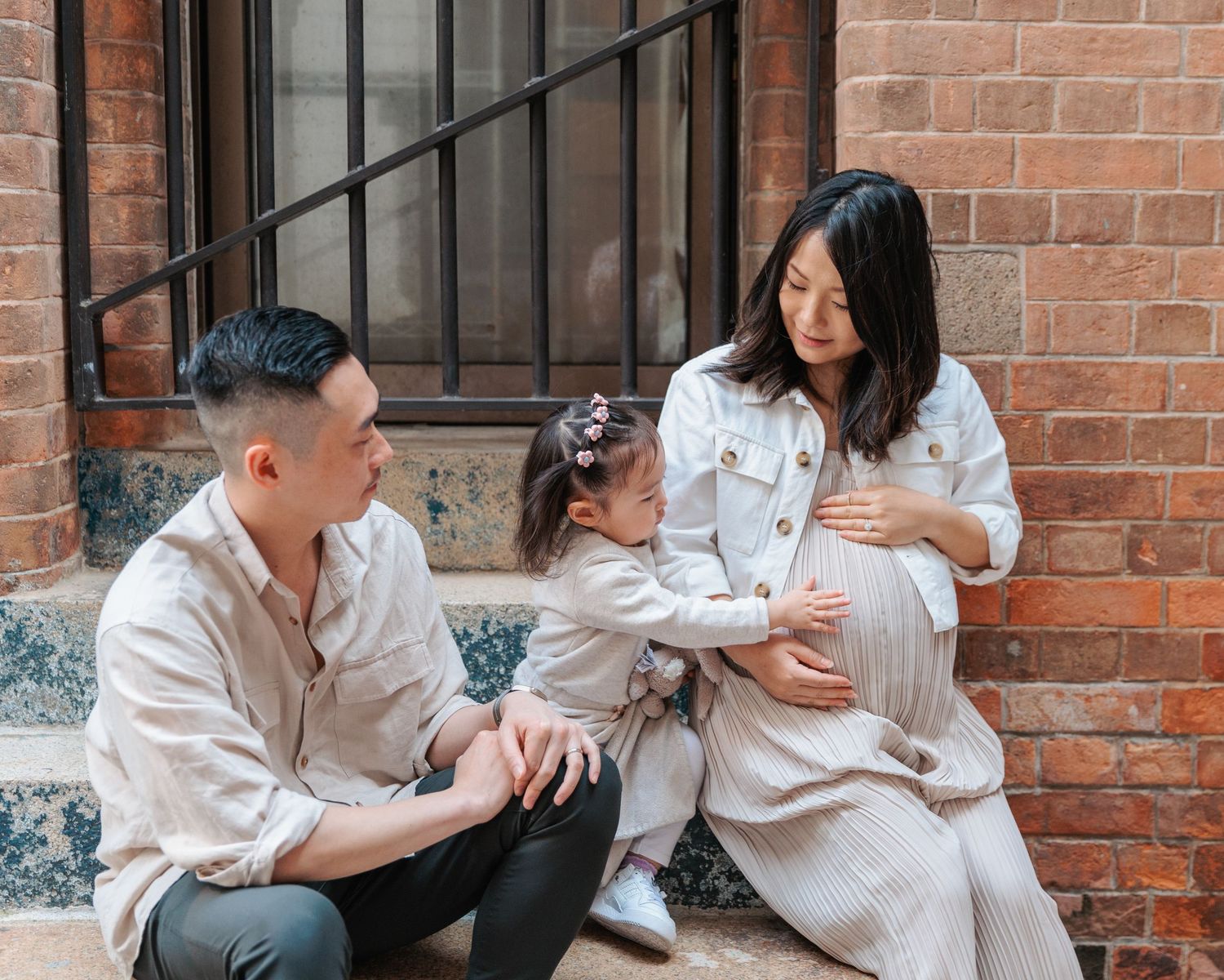 A family in matching light-colored outfits sits on brick steps together, spending quality time outdoors. Family Photoshoot in Hong Kong