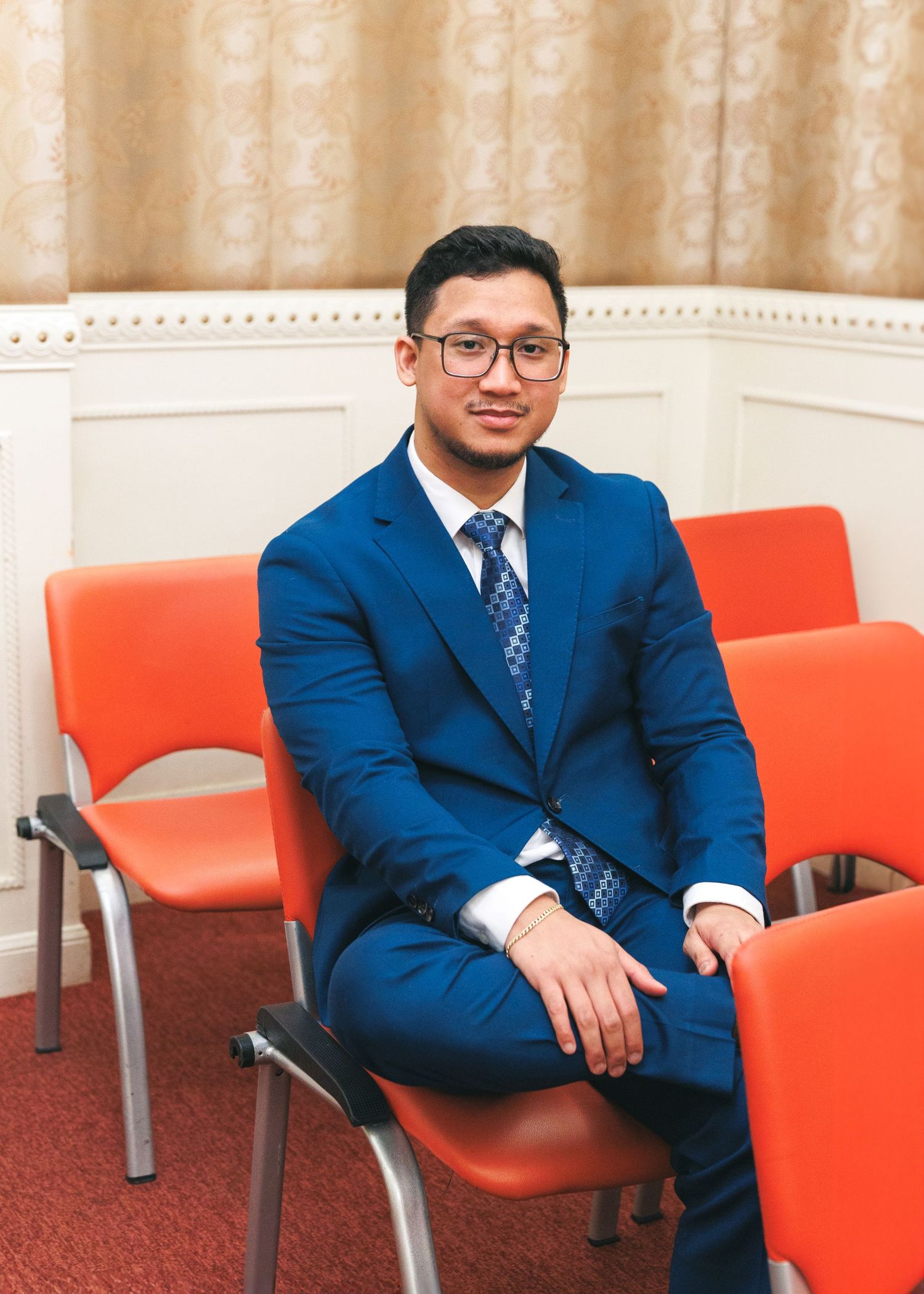 Four identical sequential images show someone in a blue suit sitting on orange chairs in a waiting area. Civil Ceremony in Hong Kong