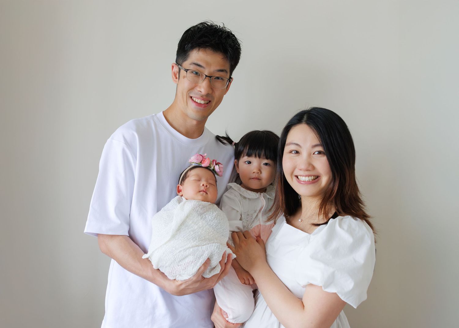 A joyful family photo series shows a couple and their baby posing together in white outfits against a neutral background. Newborn Photograph