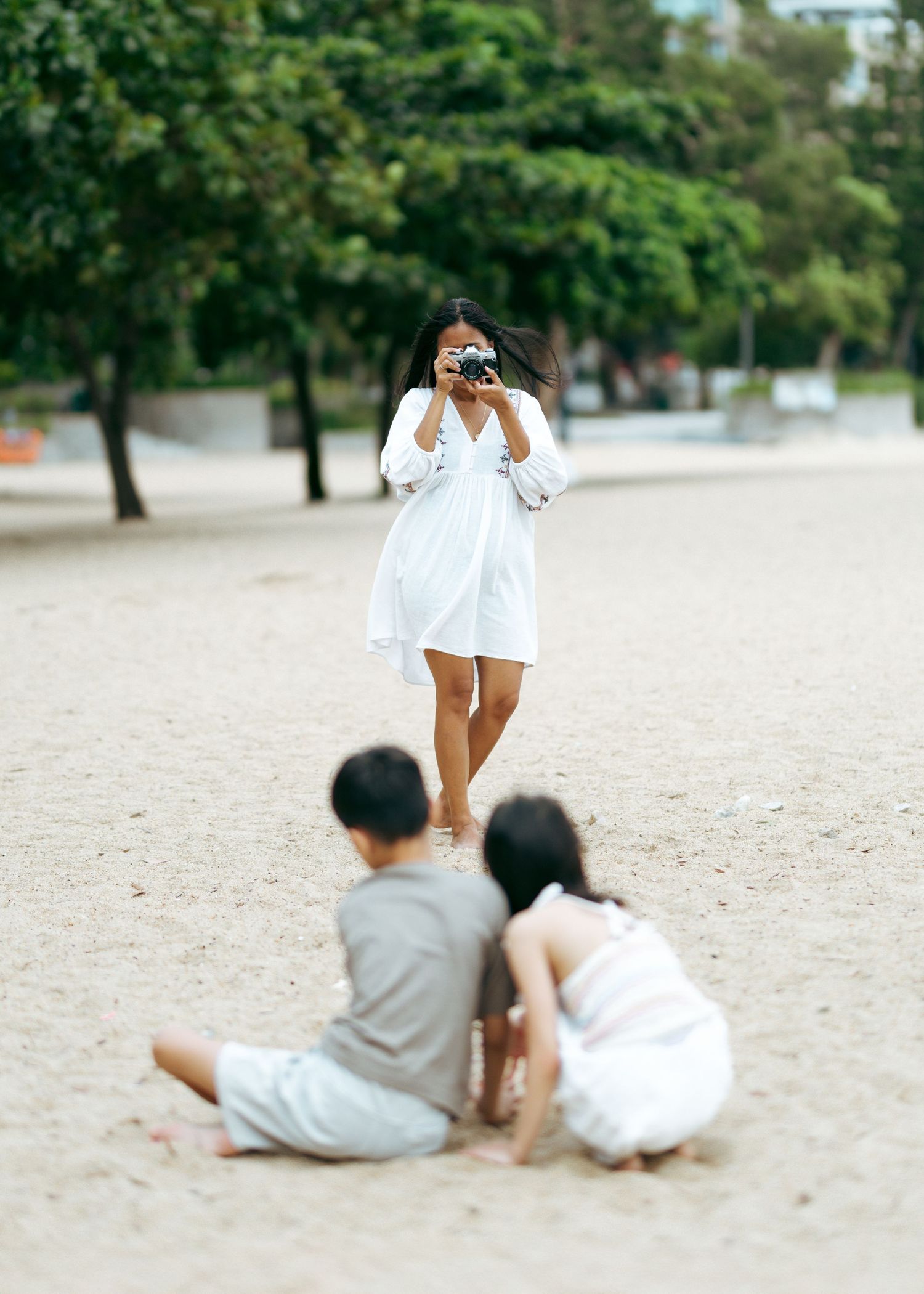 kids wearing white and gray lies on the sandy beach, showing a sequence of playful poses together. Family Photoshoot in Hong Kong