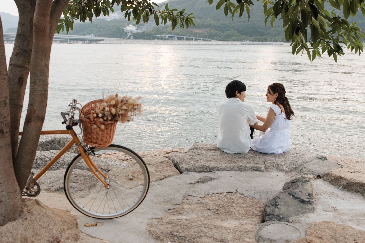 Vintage bike parked on a sandy beach surrounded by trees with a serene lake view in the background. Couple Photoshoot in Hong Kong