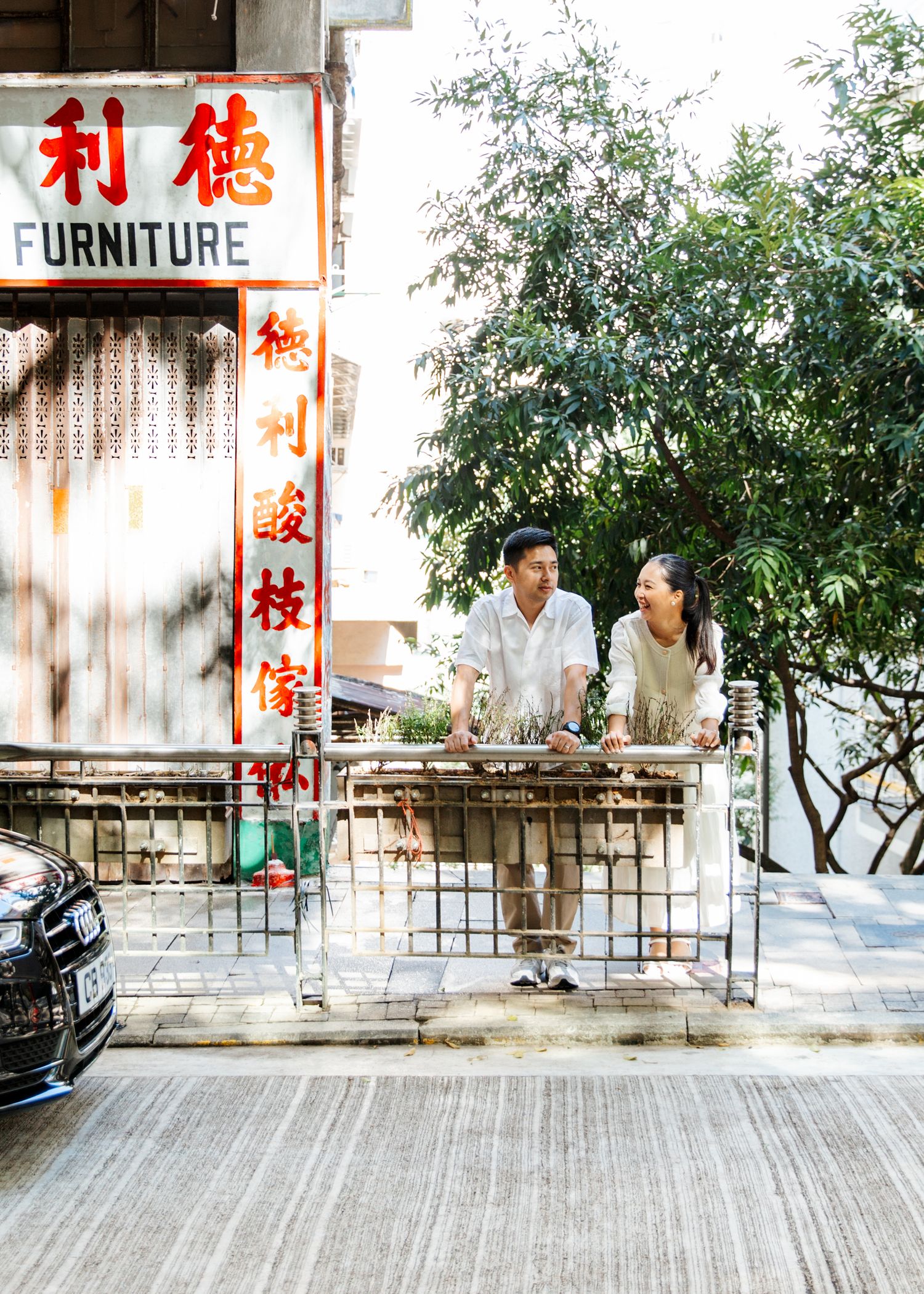 Couple in Hong Kong with Chinese signage, trees, and sidewalks in an urban setting. Couple Photoshoot in Central, Hong Kong