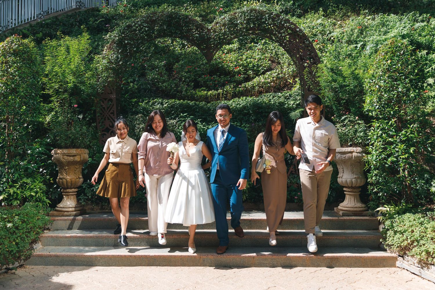 Wedding guests stand together for photos in a lush garden setting with stone archways and greenery. Civil Ceremony in Hong Kong