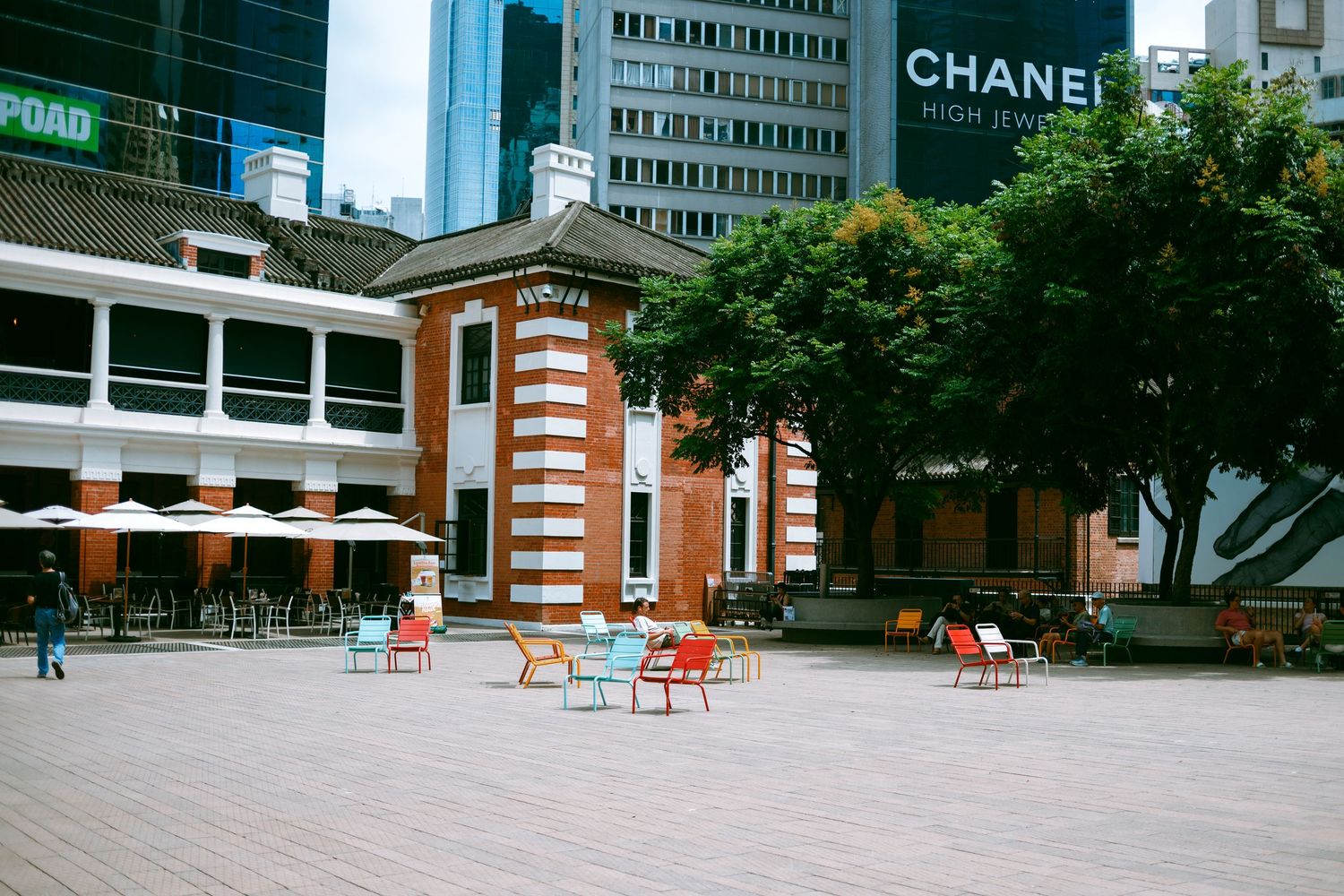 Modern urban plaza with orange chairs and historic brick building facade beneath Chanel signage in downtown setting. Taikwun, Hong Kong