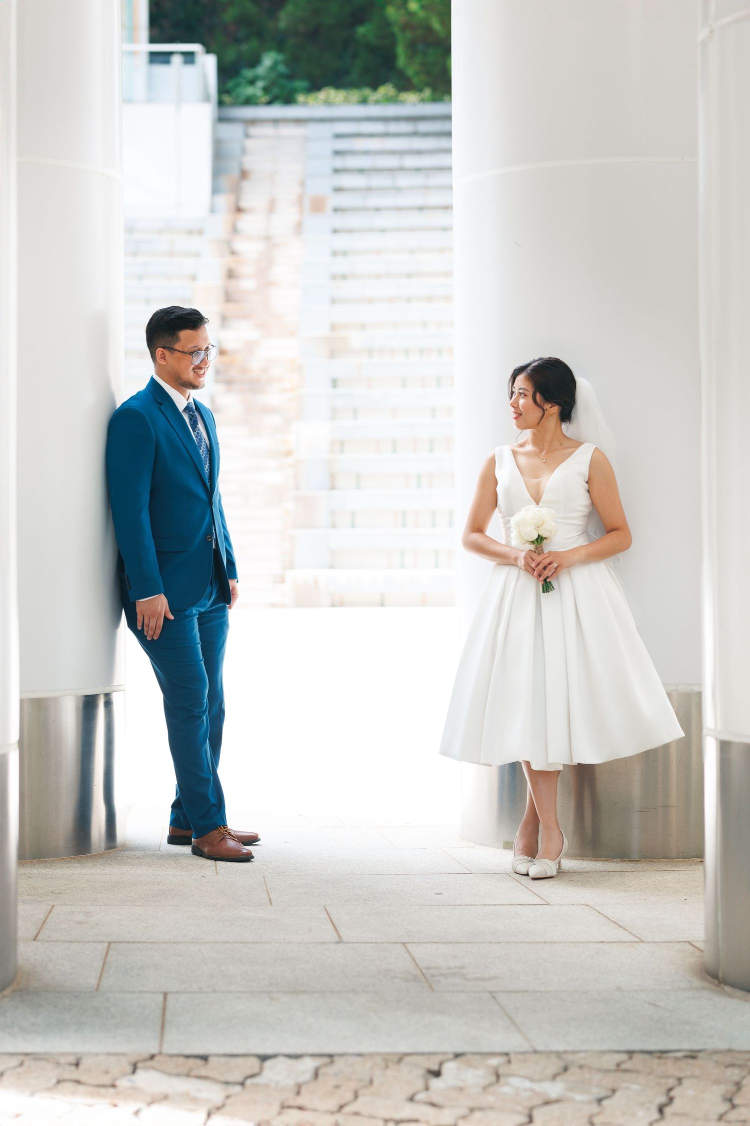 A couple takes portraits in a white columned hallway, with the bride in a short white dress and groom. Civil Ceremony in Hong Kong
