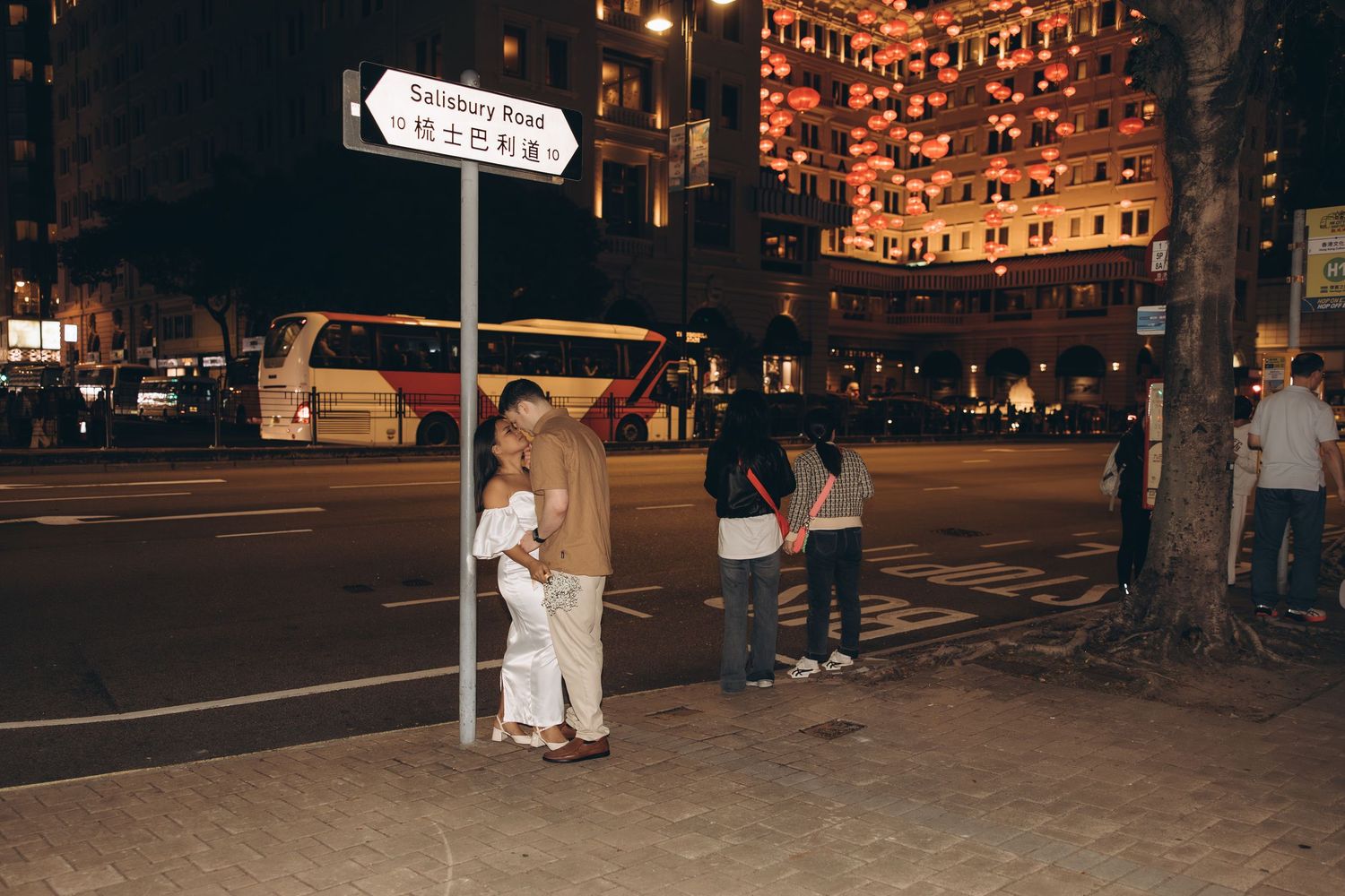 A dark cityscape photo shows couple walking across an illuminated crosswalk at night. Couple Photoshoot in Hong Kong