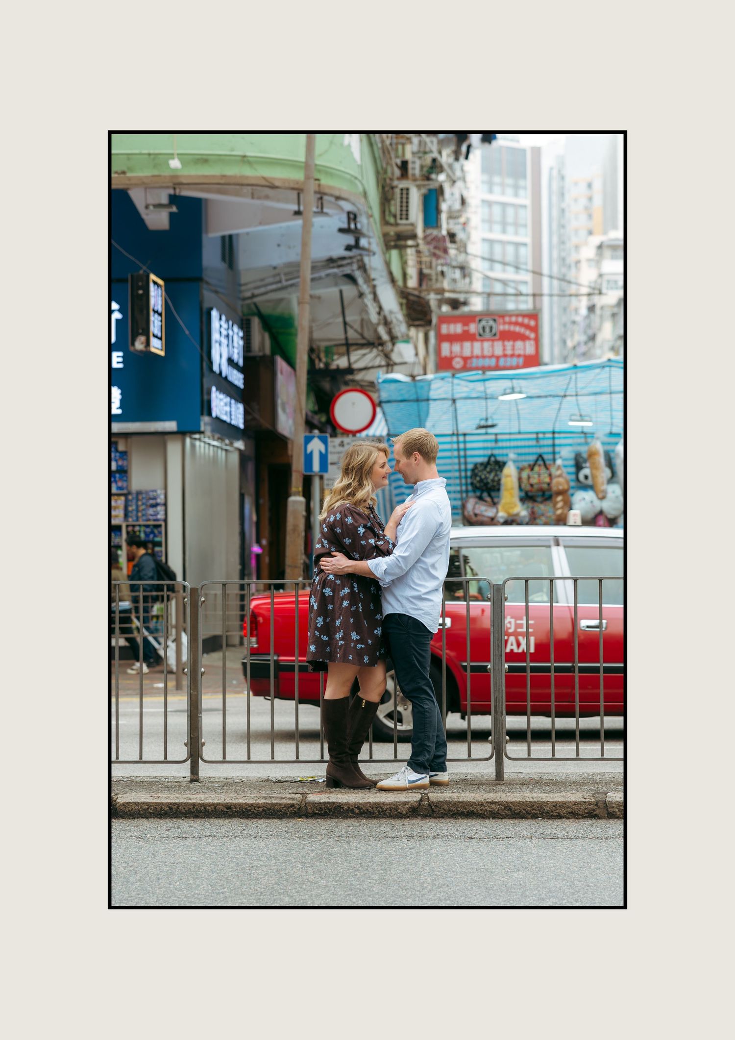 Couple embracing on a busy Hong Kong street corner with red taxi and colorful signs in the background. couple session in Hong Kong.
