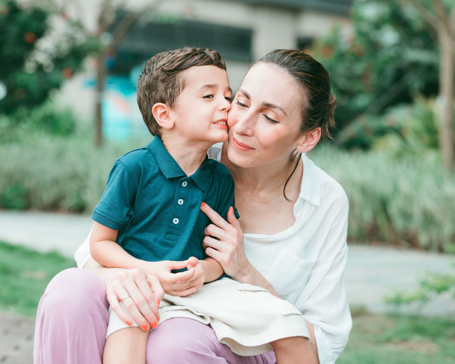 A tender moment shared between a child in a blue polo and an adult outdoors in a garden setting. hong kong family photographer