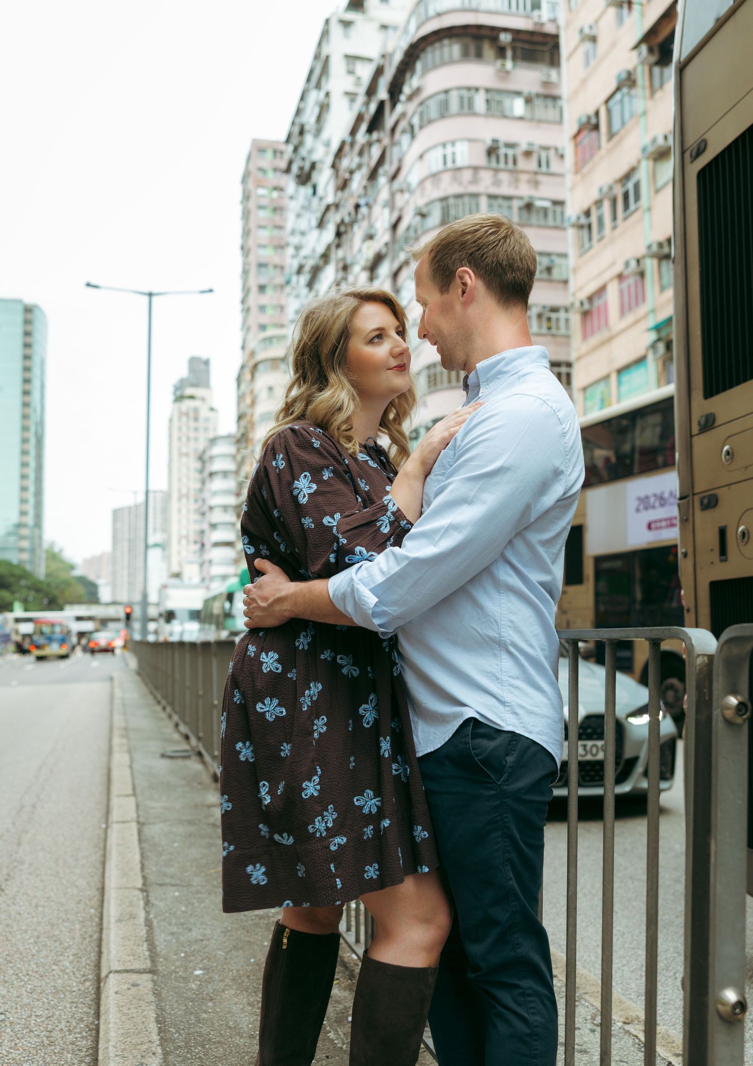 A couple embraces romantically on a city sidewalk in Hong Kong, with colorful high-rise buildings in the background. couple session in HK