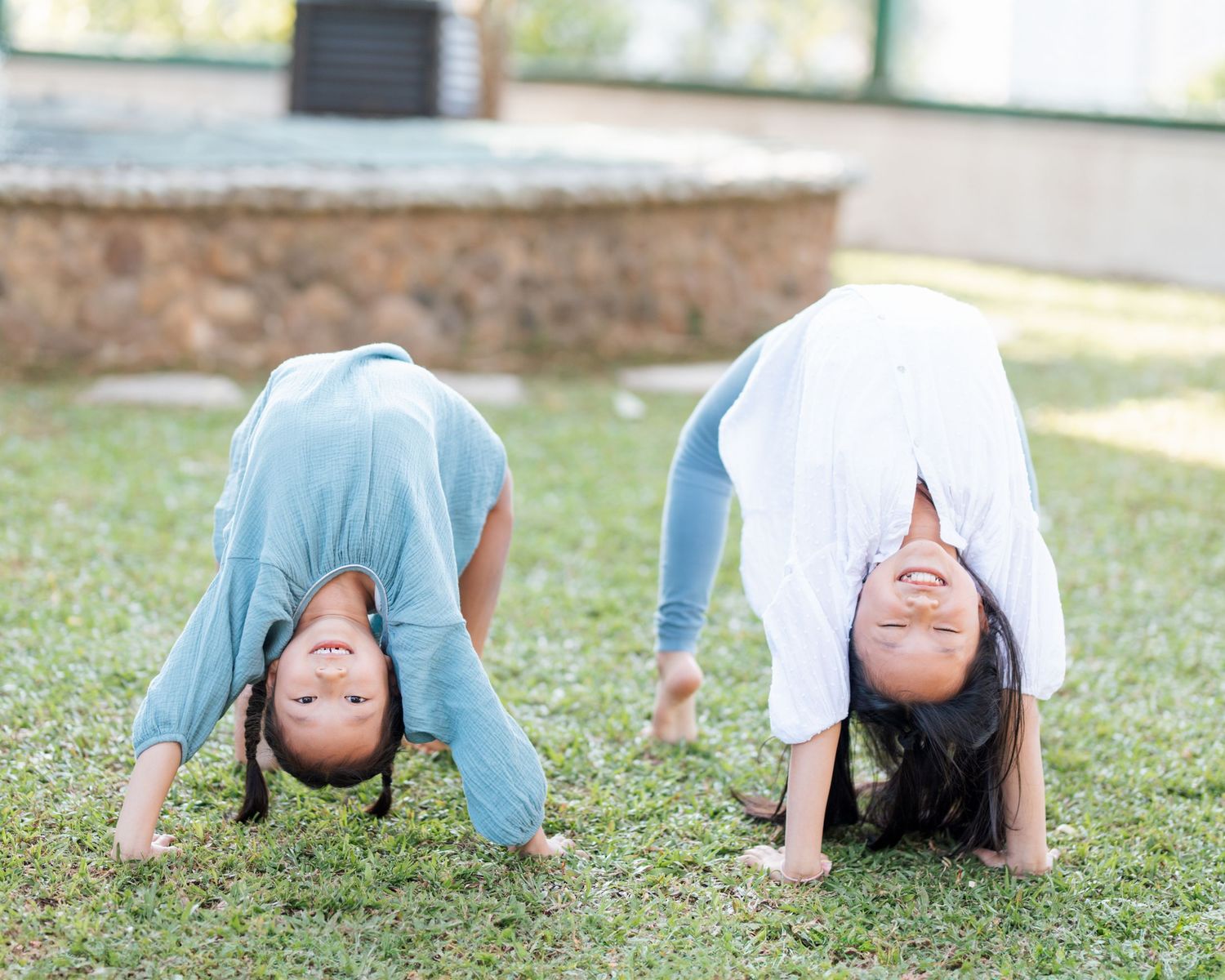 Two children having fun doing backbends on grass in blue and white clothes while playing outdoors together. Hong Kong Family Photographer