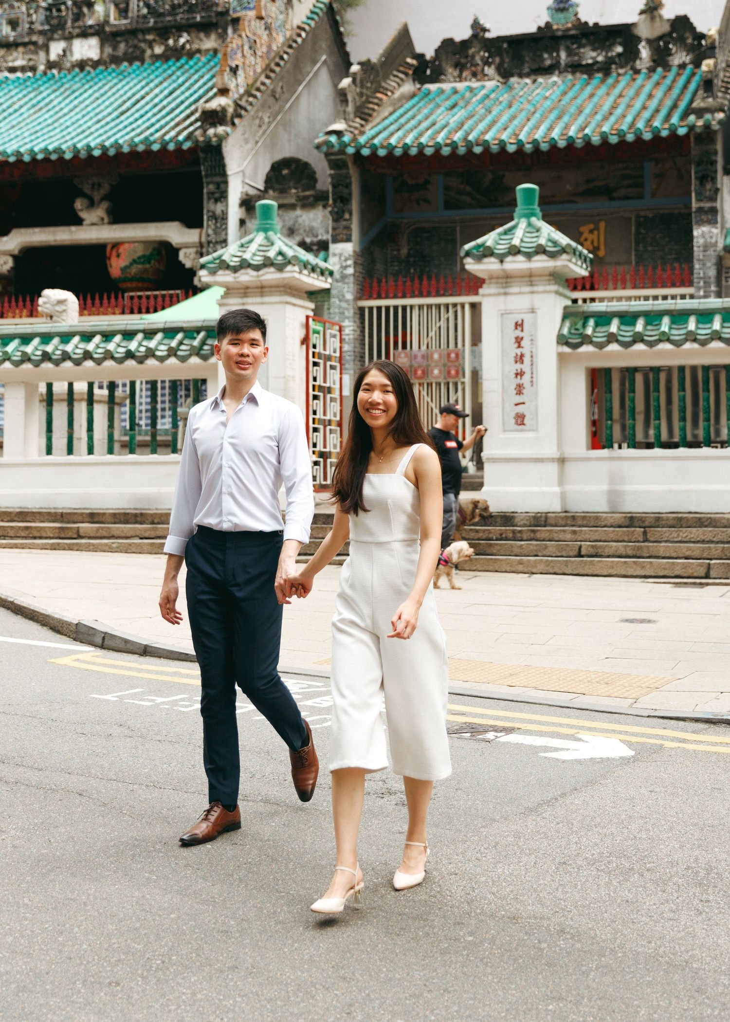 A couple walks together in front of a traditional Chinese temple with turquoise roofs in Hong Kong. Couple Photoshoot in Hong Kong