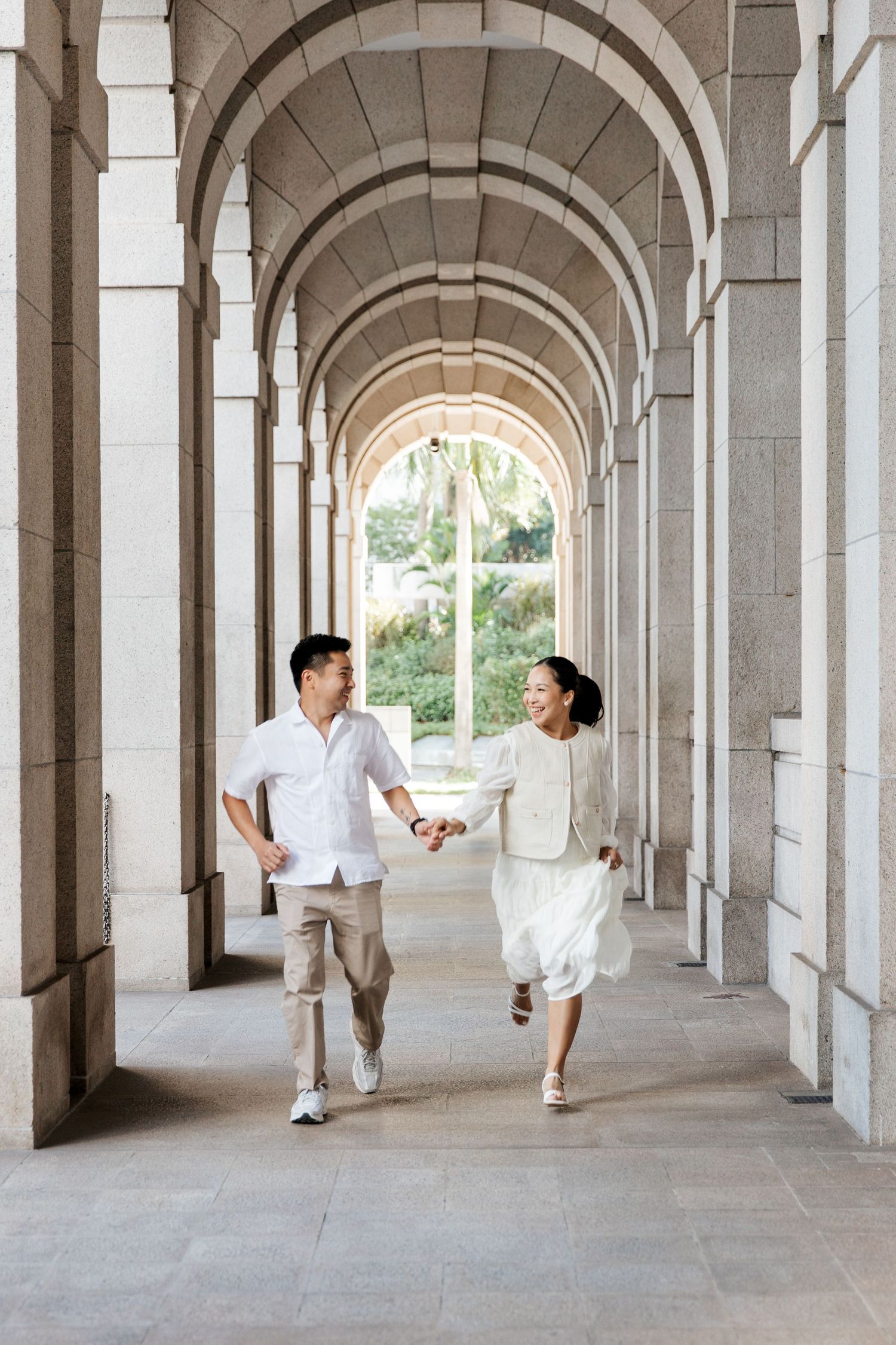 couple in white outfits dance gracefully through a long arched stone colonnade in Central, Hong Kong, pre-wedding photoshoot