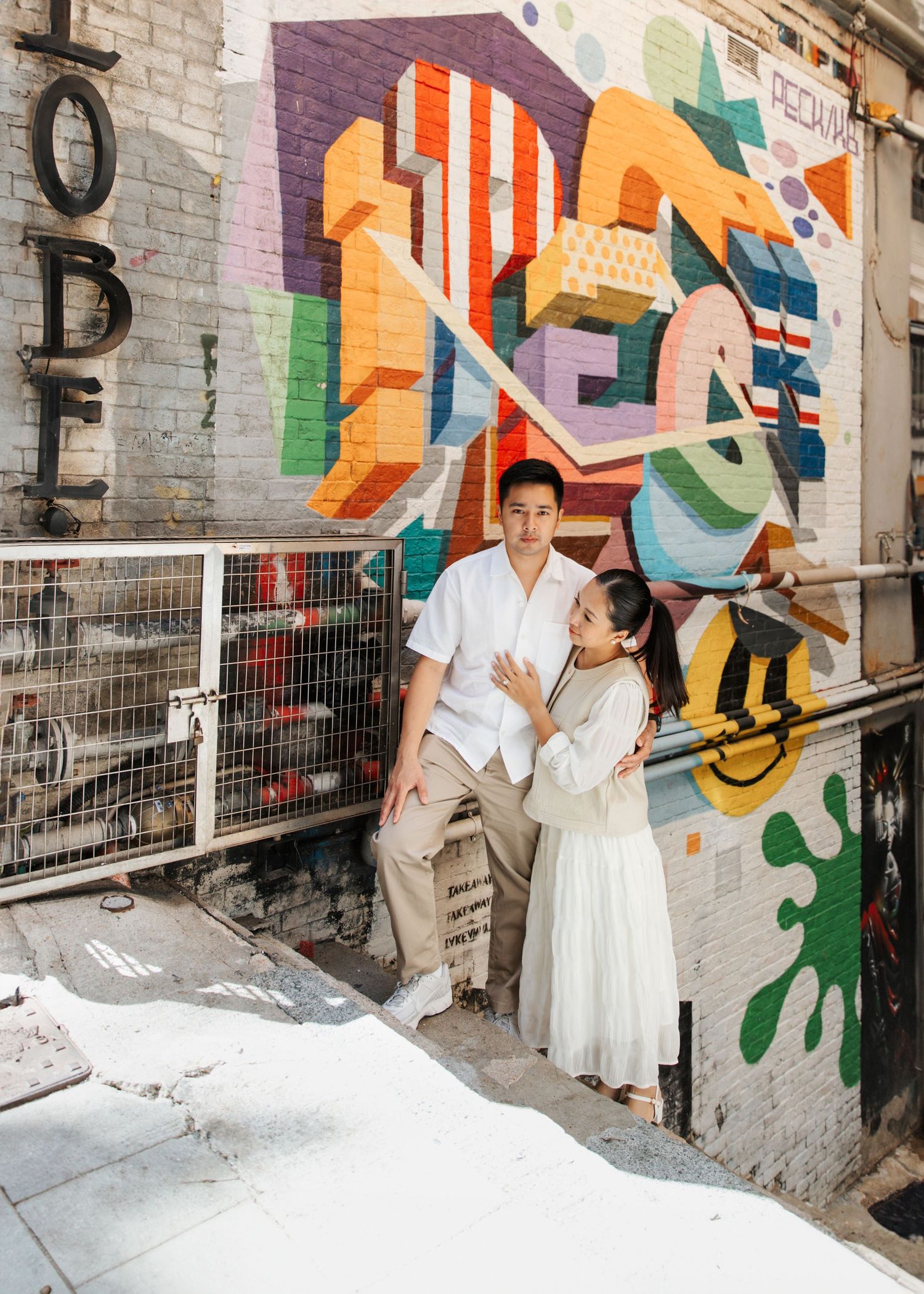 couple stand together against a vibrant graffiti wall in an alleyway. Couple Photoshoot in Central, Hong Kong