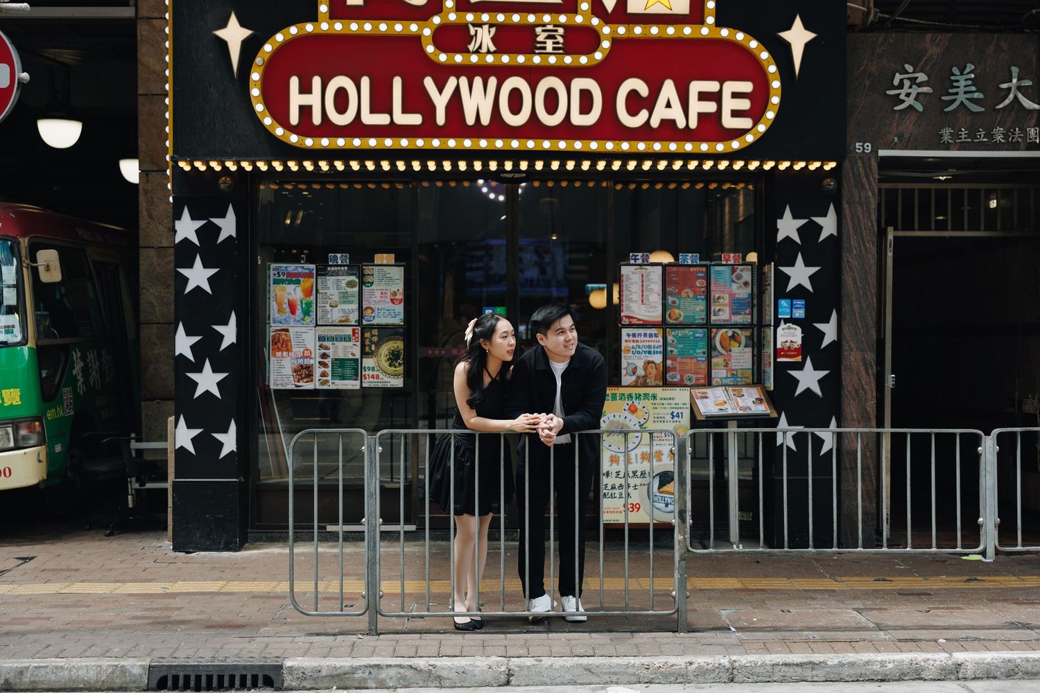 People stand outside the iconic Hollywood Cafe's neon sign glowing in the city street at night. Couple Photoshoot in Hong Kong