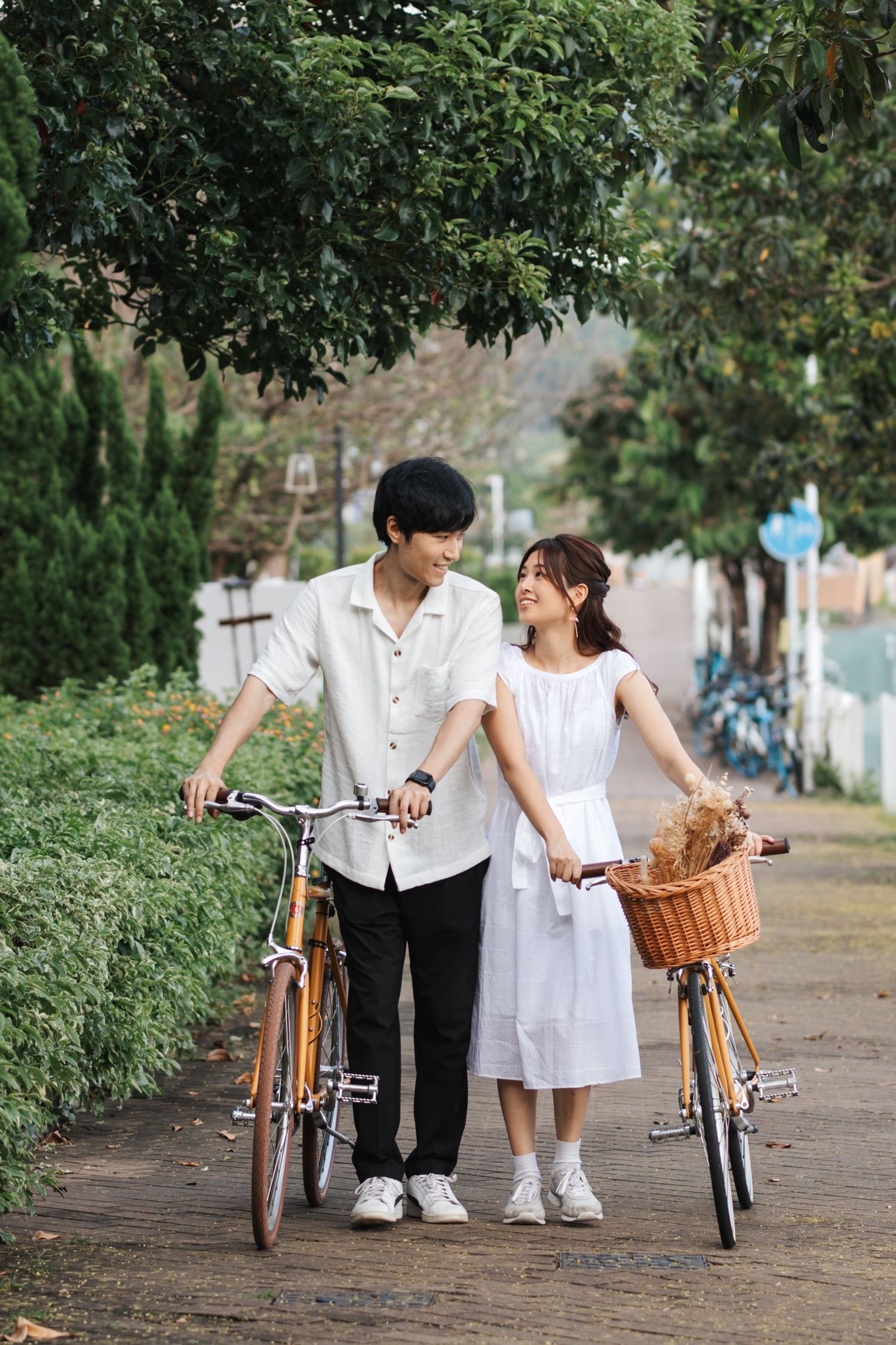 Two children in white outfits standing together with vintage bicycles on a tree-lined path. Couple Photoshoot in Hong Kong