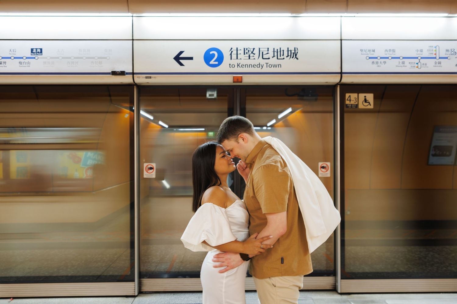 couple wait on a crowded subway platform with blurred motion during rush hour in Hong Kong.  Couple Photoshoot in Hong Kong