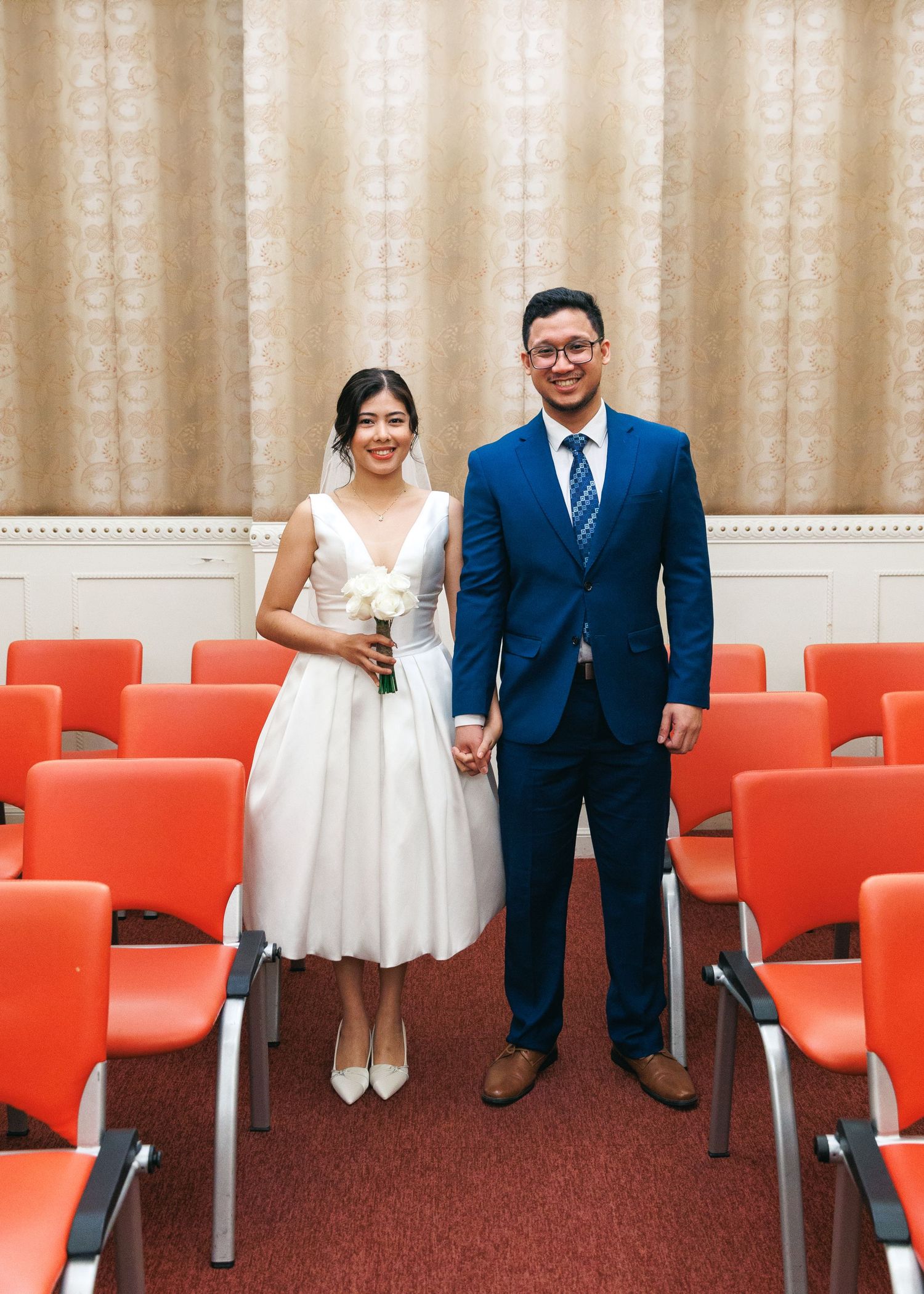 Wedding party seated on bright orange chairs against beige curtains in a formal event space. Civil Ceremony in Hong Kong