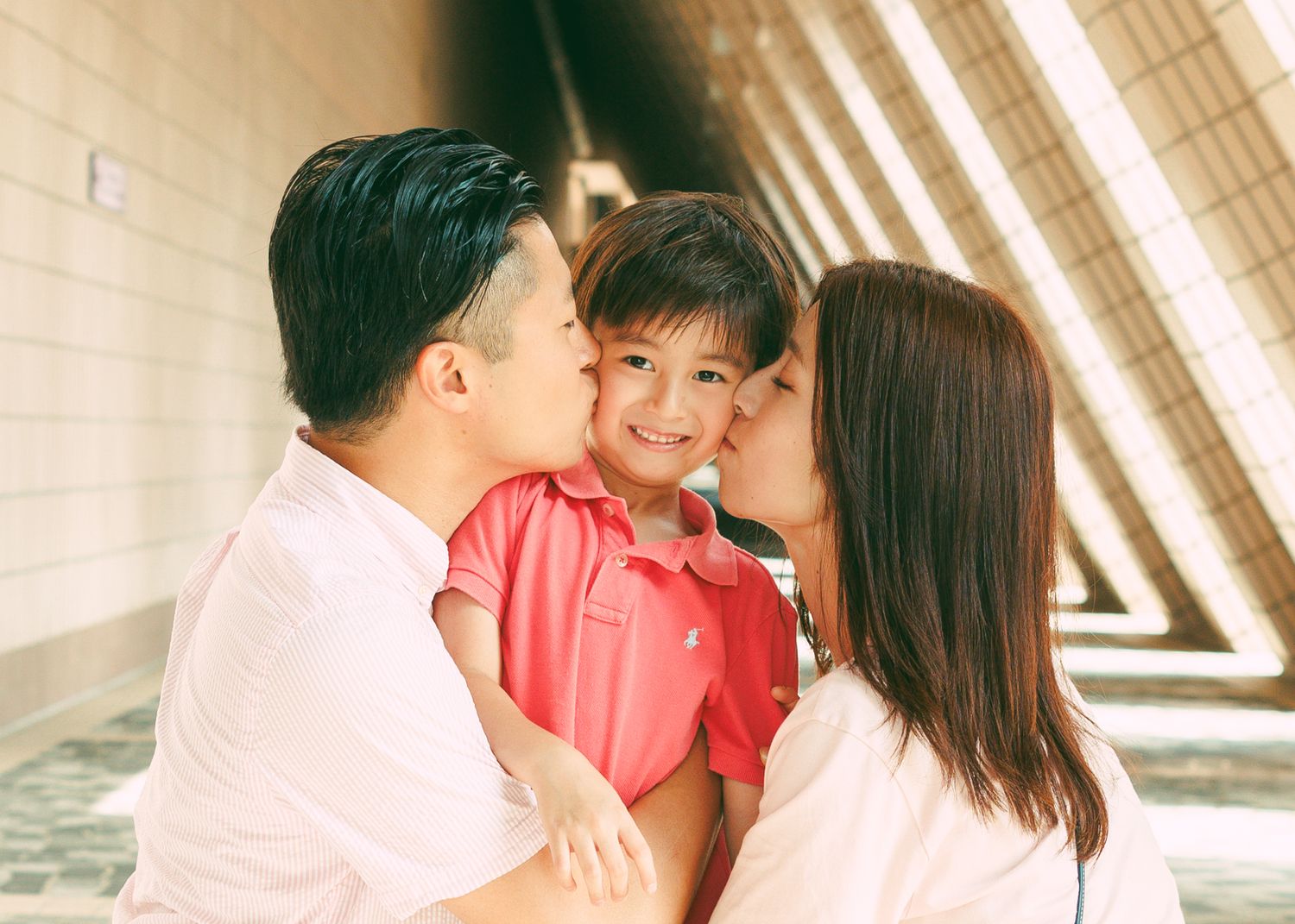 A loving family shares a tender moment together in a hallway with angular architectural lines and natural lighting. Family Photoshoot in HK