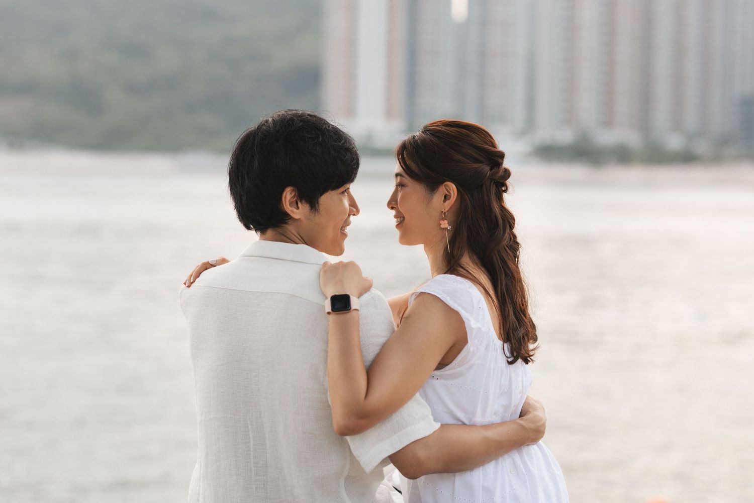 Couple in white outfits sharing romantic embraces and kisses along a misty beach shoreline. Couple Photoshoot in Hong Kong