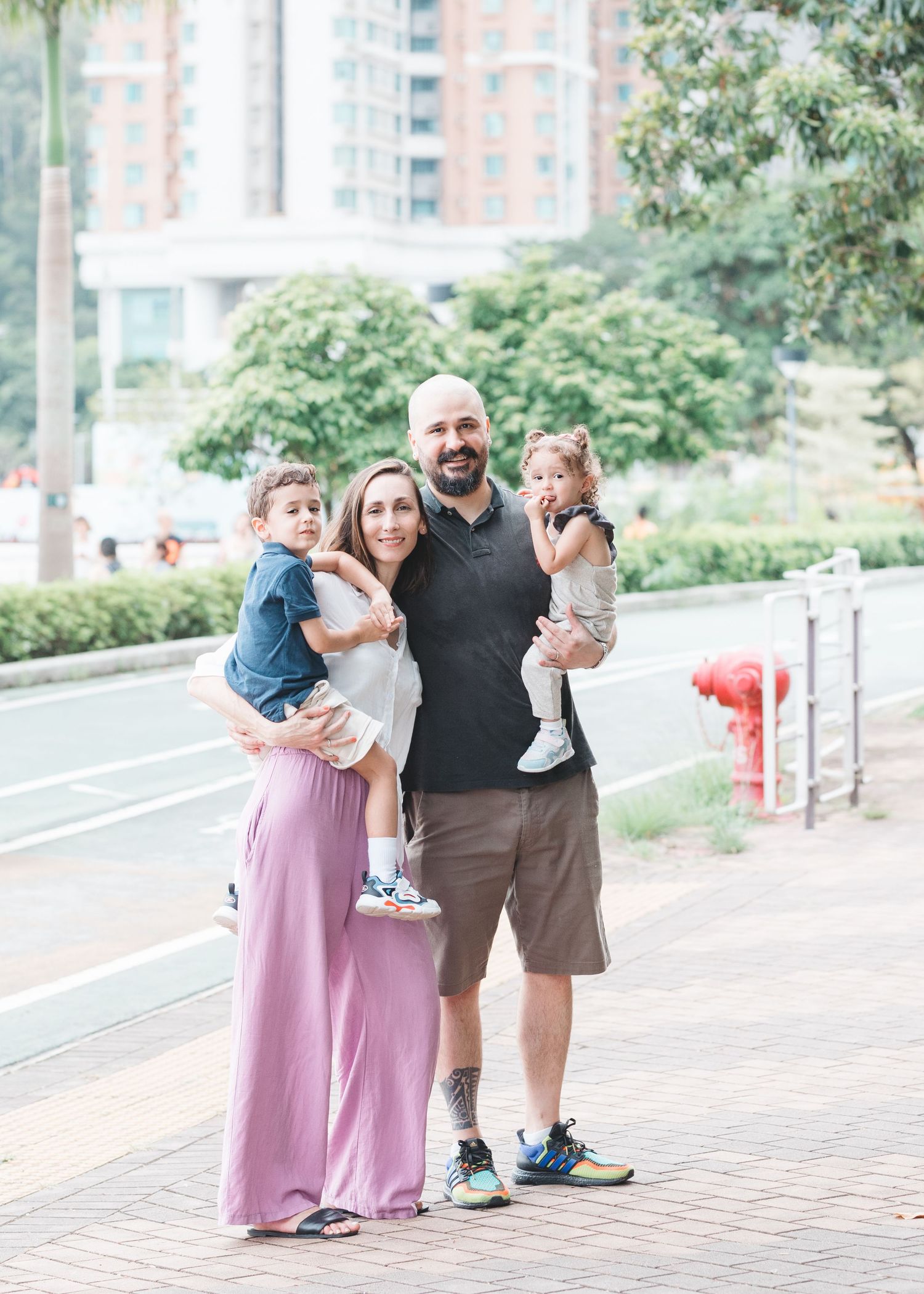 A series of candid family moments on a brick walkway with city buildings in the background. Family Photographer in Hong Kong