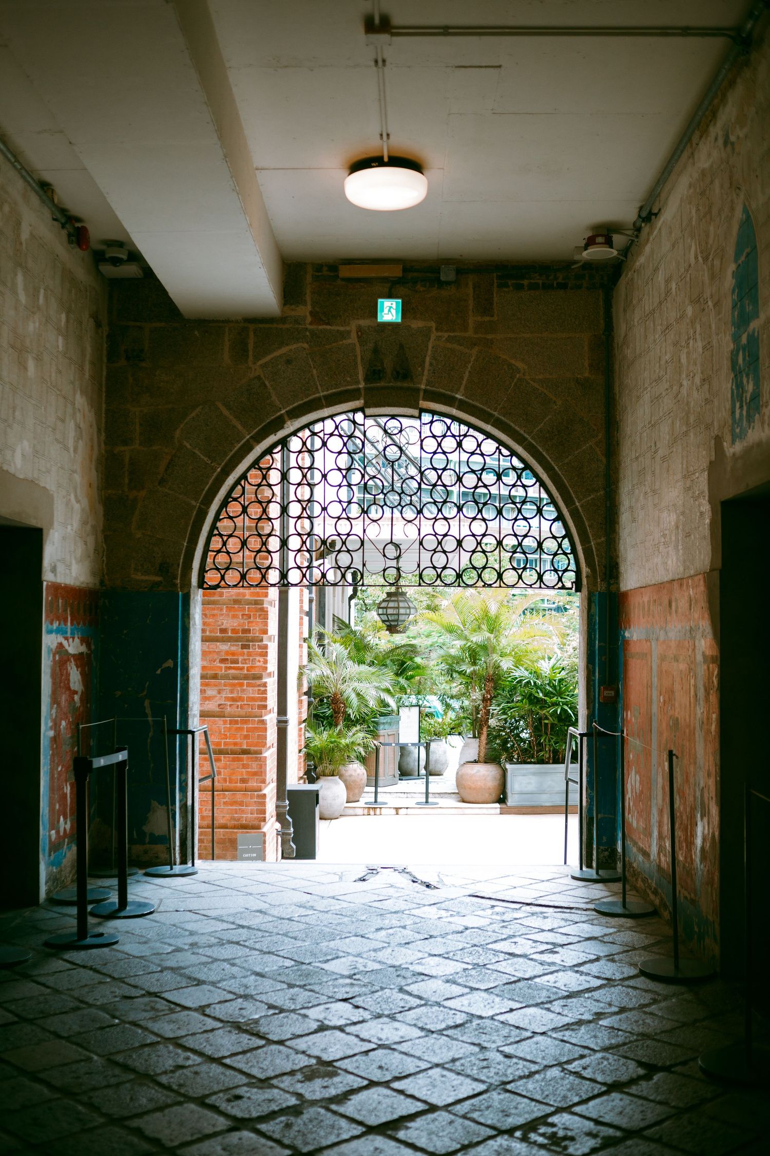 Stone archway tunnel in an old industrial building with a patterned iron gate and natural light streaming through. Taikwun, Hong Kong