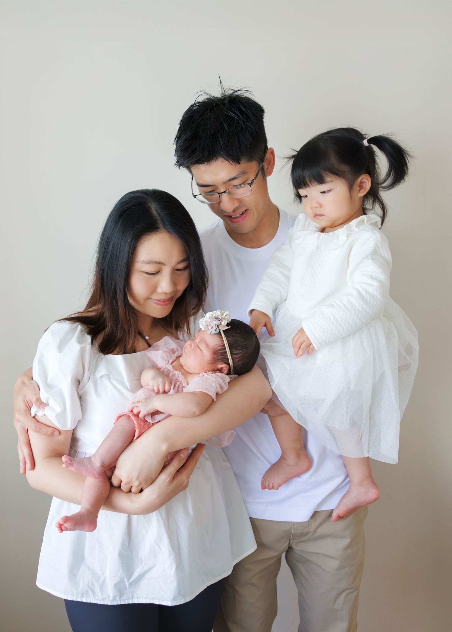 Four connected photos show a family in white shirts holding and interacting with a baby in pink  Newborn Photography in Hong Kong