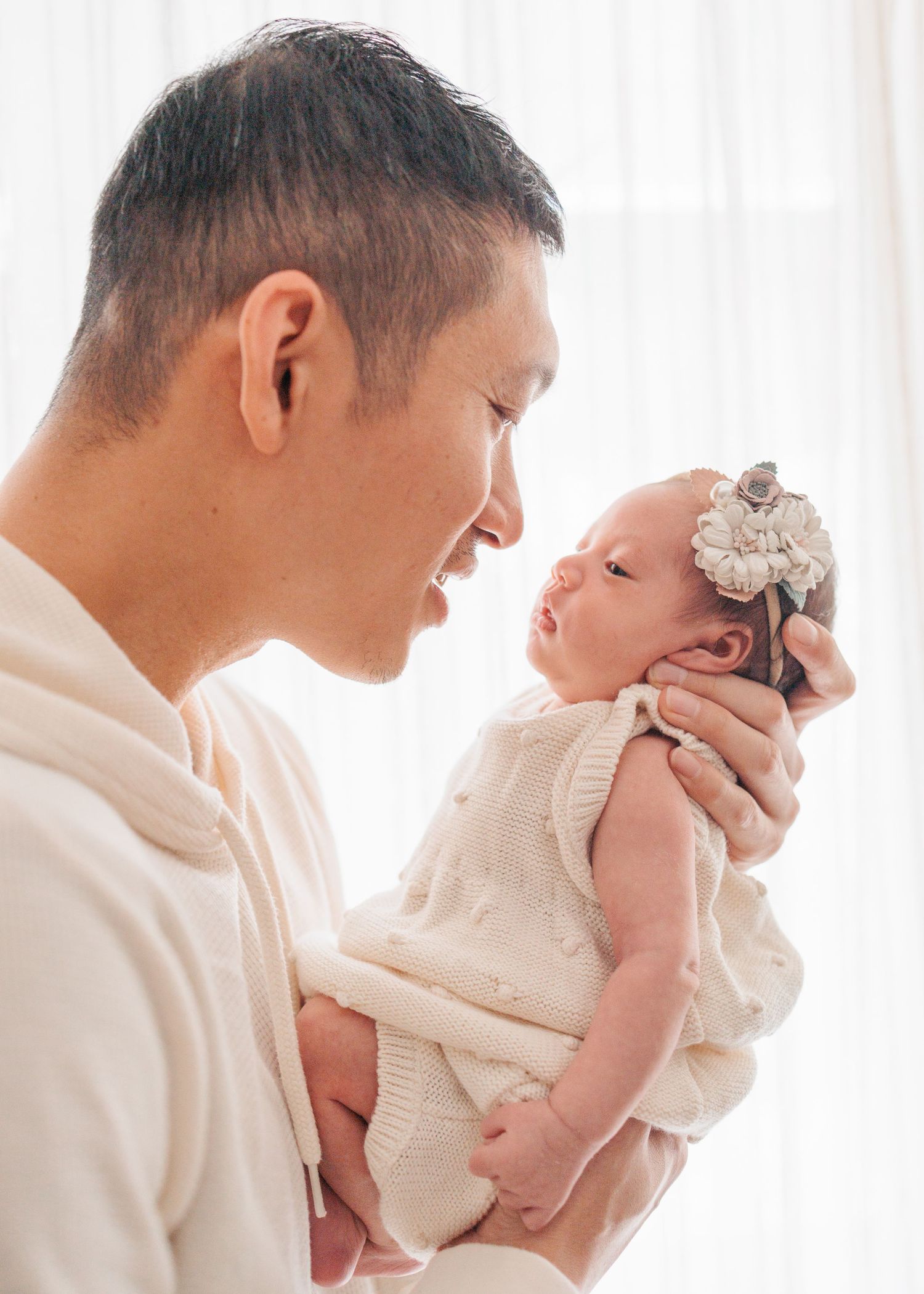 A tender moment captured in progression as a parent lovingly lifts and nuzzles a small baby wearing white. In-home newborn session in HK