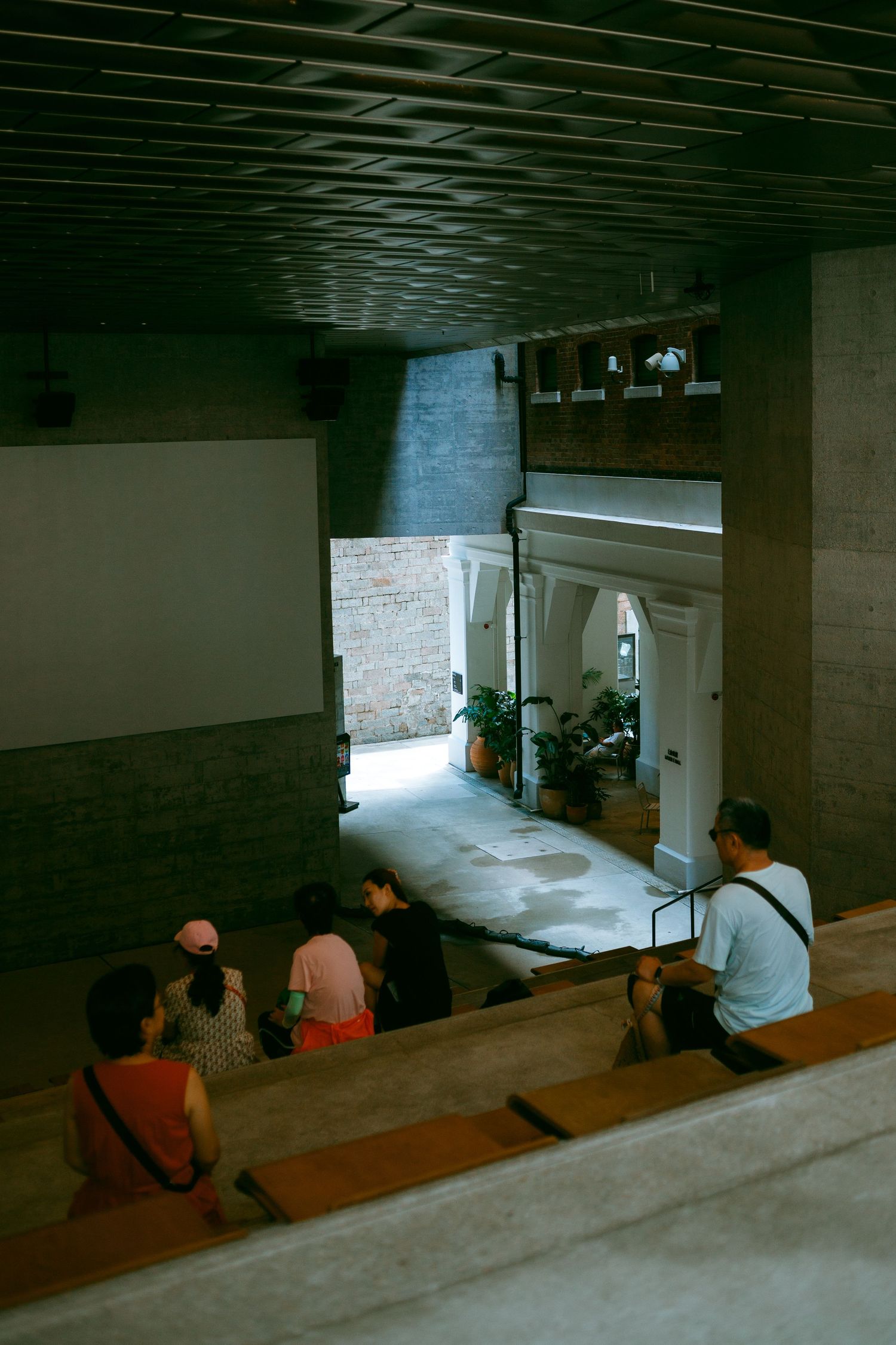 Dark basement interior shows three people sitting in a row on wooden seating while watching a screen in low light. Taikwun, Hong Kong