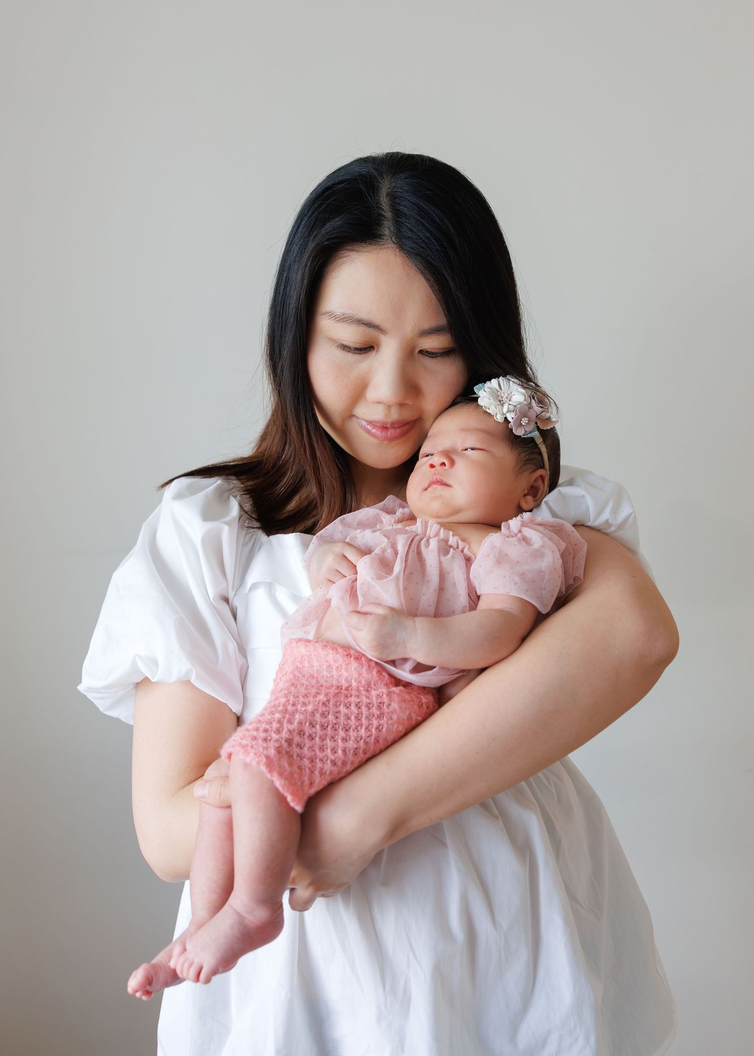 A heartwarming series of photos showing tender moments between a mother wearing white and her baby in pink Newborn Photoshoot in Hong Kong