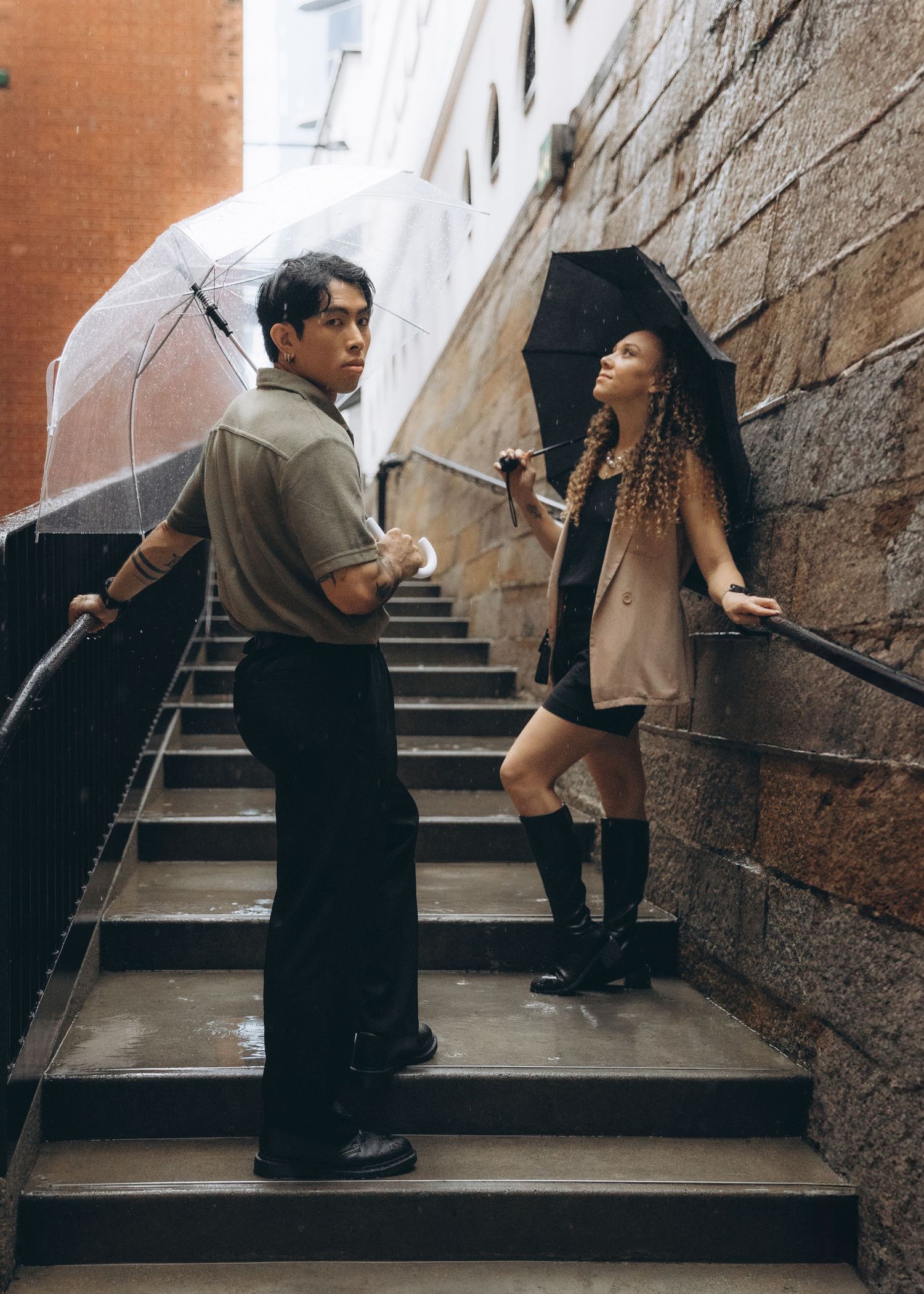 Couple in dark clothing ascend stone steps in a narrow passageway between brick and stone walls. Pre Wedding in Hong Kong