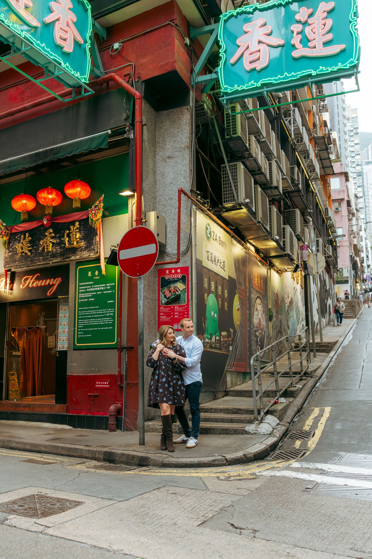 Couple embracing on a Hong Kong street corner with neon signs and red lanterns outside a traditional restaurant. couple session in Hong Kong