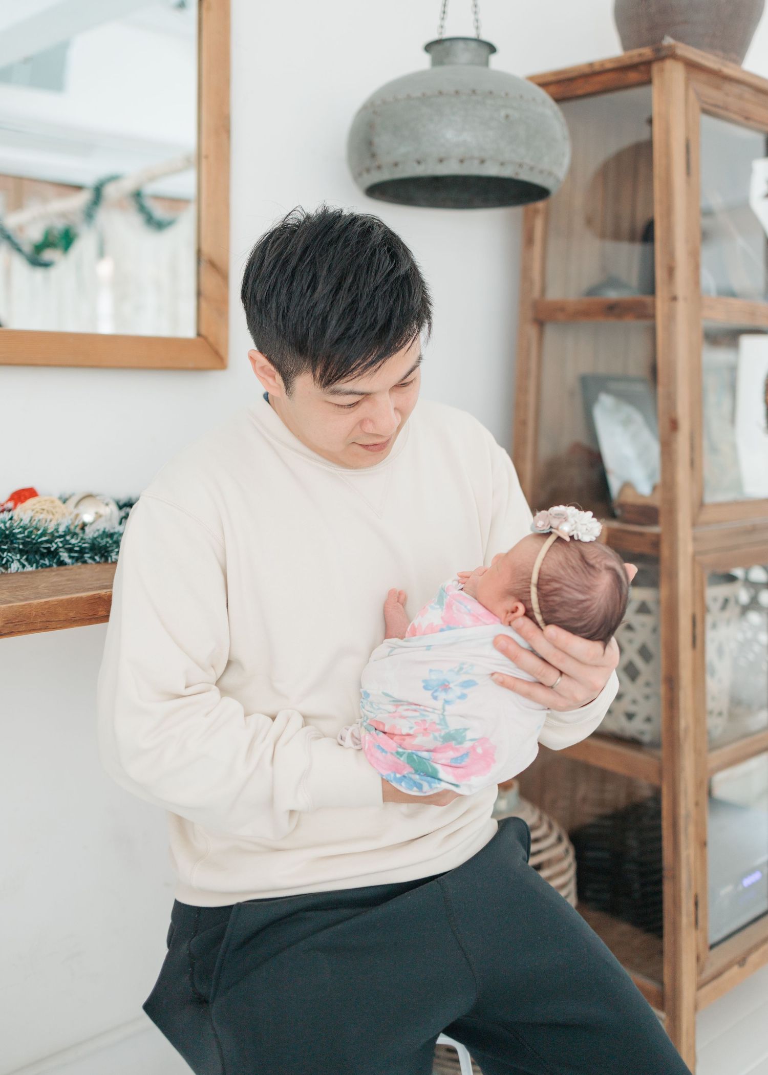A parent in a white sweater gently feeds and bonds with their baby while sitting on a cozy gray couch. Newborn Photographer in Hong Kong