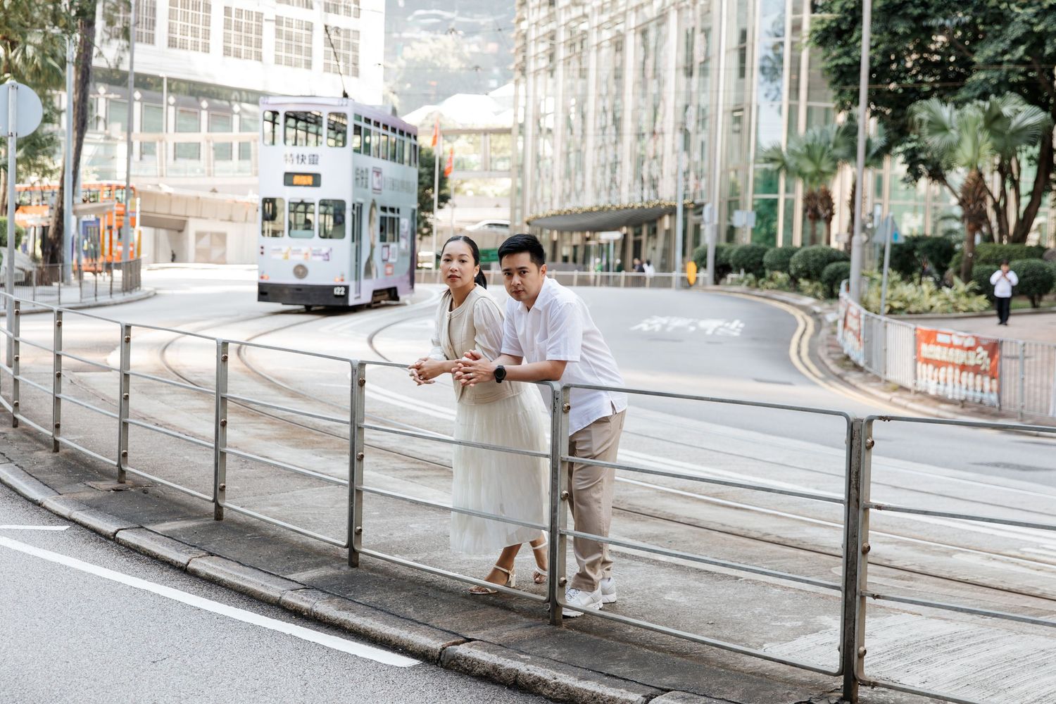 A series of couple waiting at a tram stop along a modern urban street with overhead cables. Couple Photoshoot in Central, Hong Kong