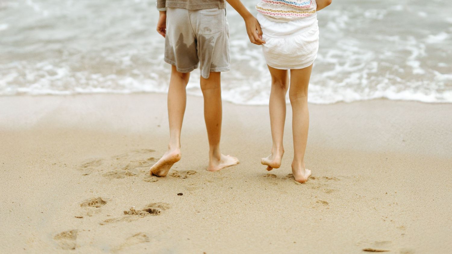 Two pairs of bare legs and feet standing in wet sand at the beach with ocean waves visible in the background. Family Photoshoot in Hong Kong