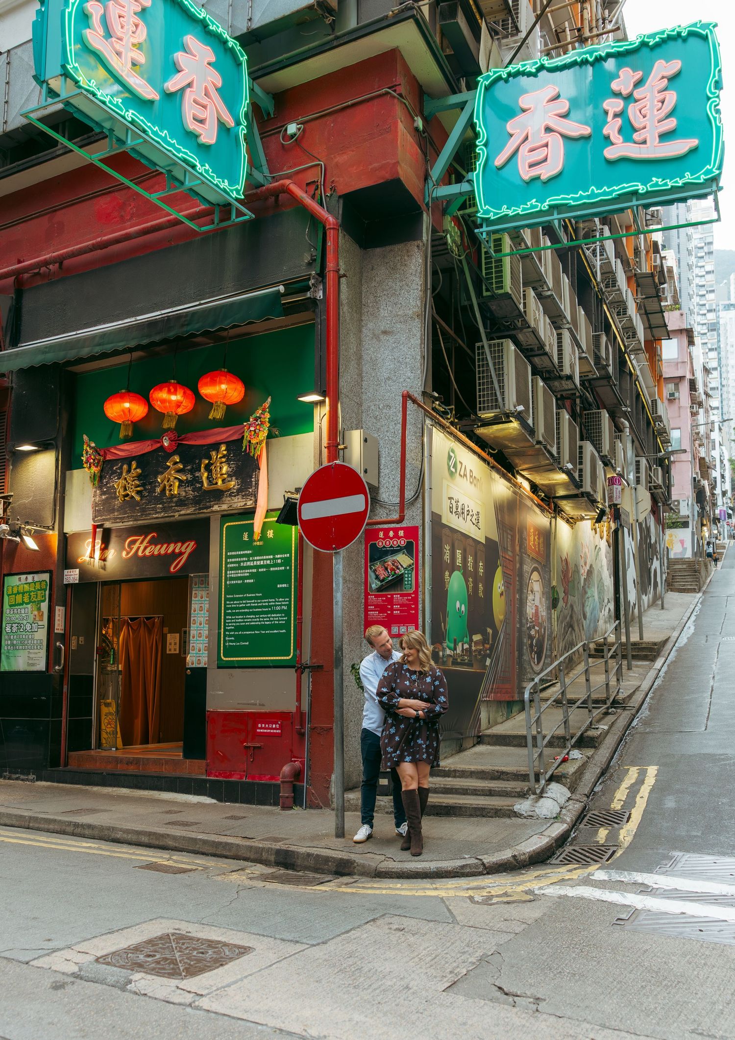 Couple standing outside a traditional Hong Kong shop with green Chinese signs and red lanterns on a narrow city street. couple session in HK
