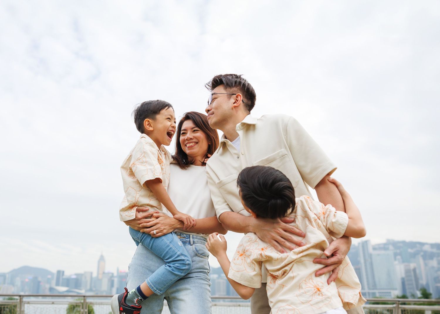 A joyful family enjoys quality time together while overlooking a city skyline on an overcast day. Hong Kong Family Photographer