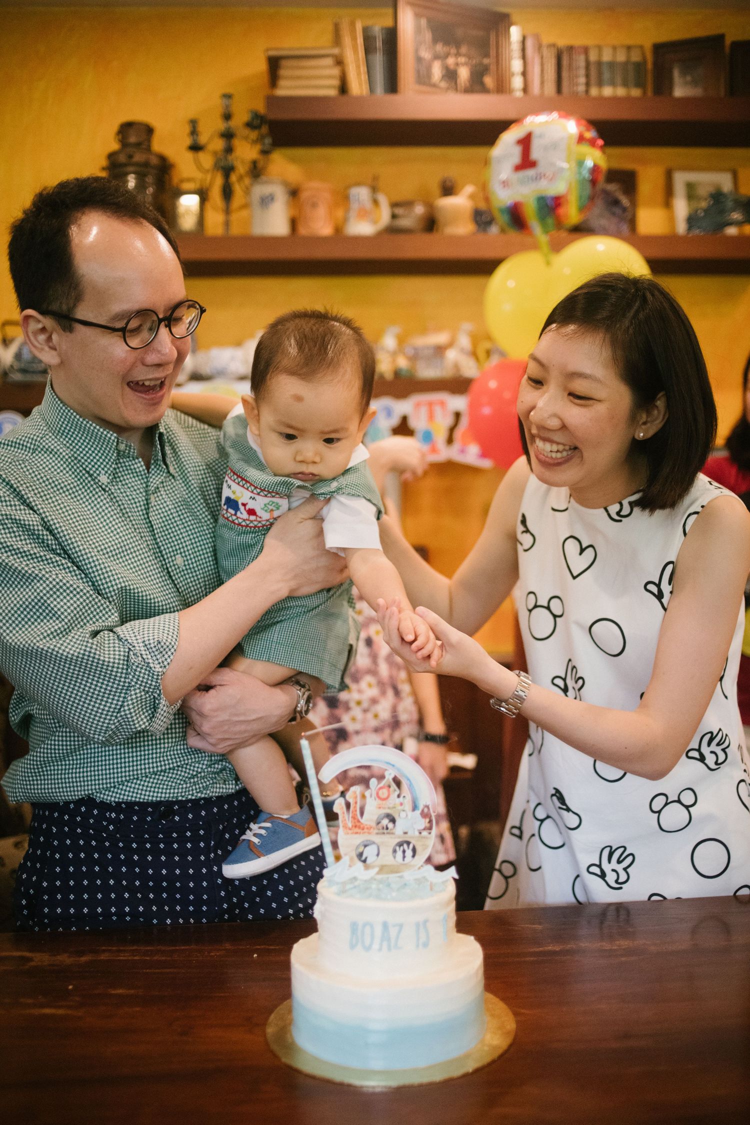 A family celebrates their baby's first birthday with a cake and balloons in a cozy home setting. Family Photoshoot in Hong Kong
