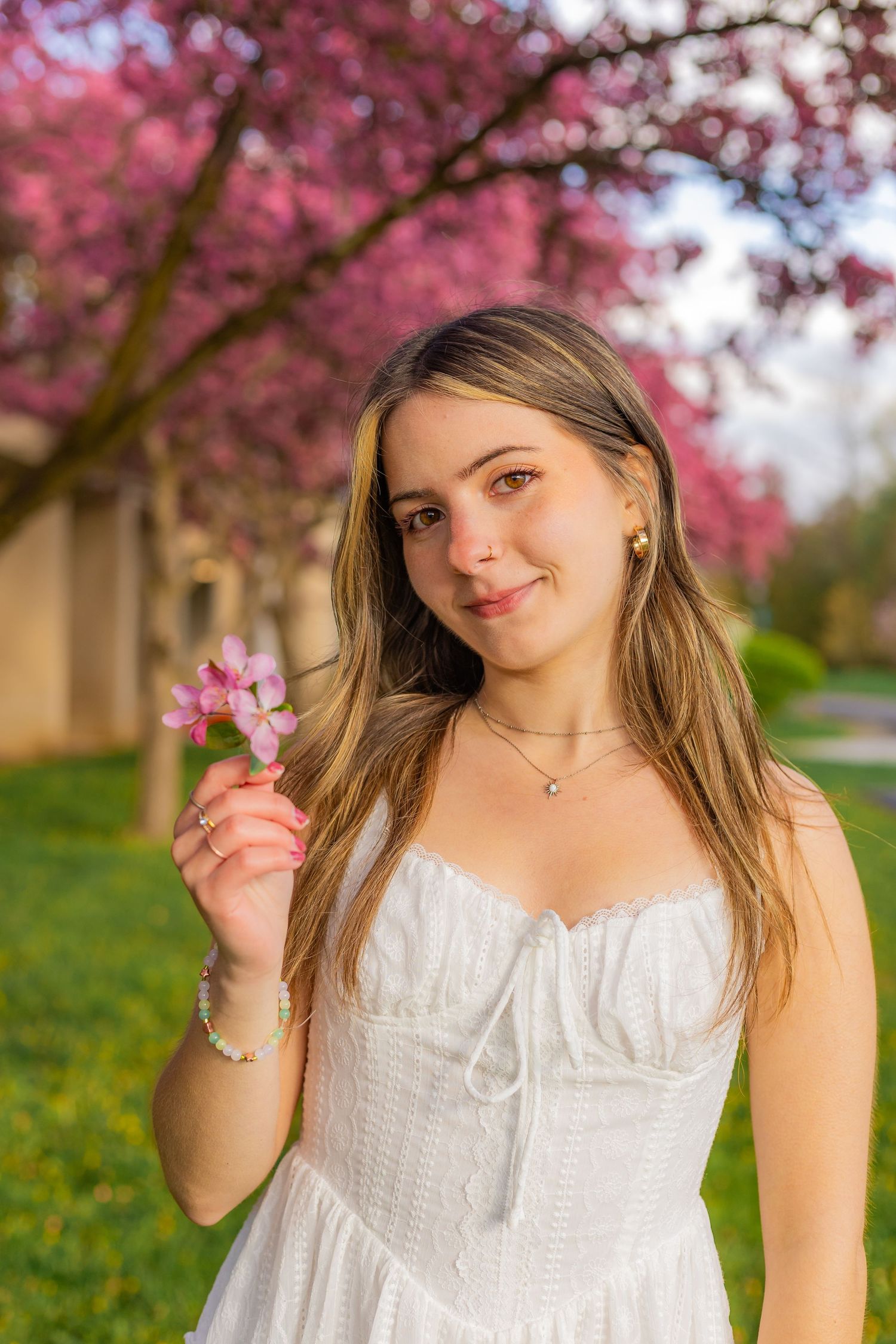 a young woman holds a small branch of cherry blossoms, standing in front of a pink cherry tree