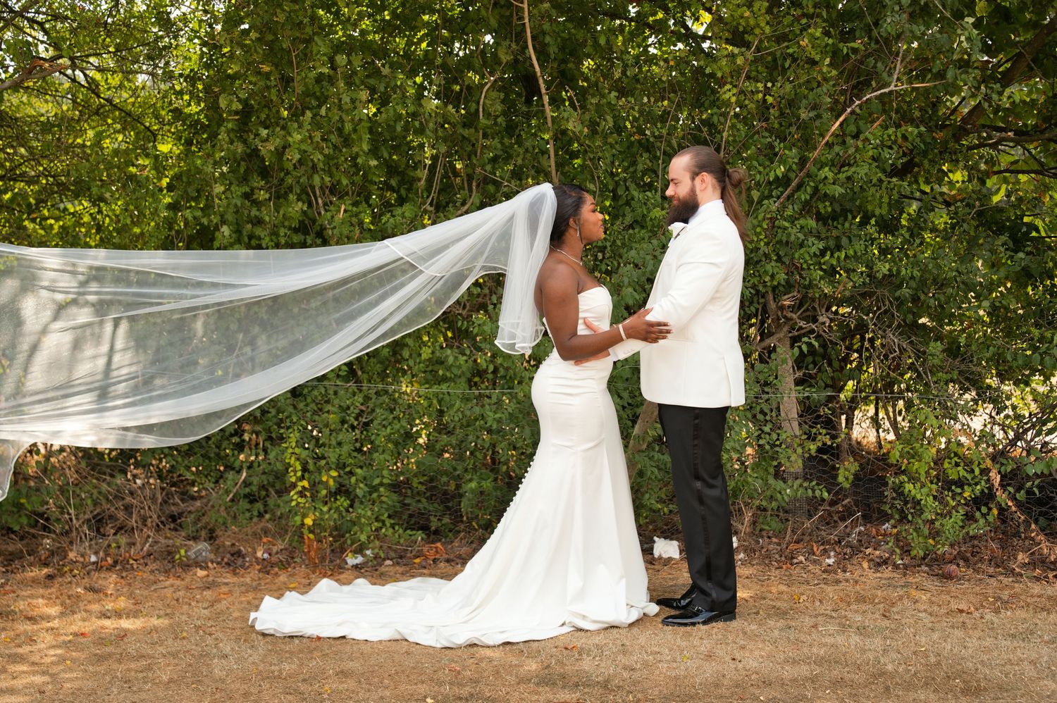 Adonis and Rachel standing together beneath a flowing veil in the garden on their wedding day.