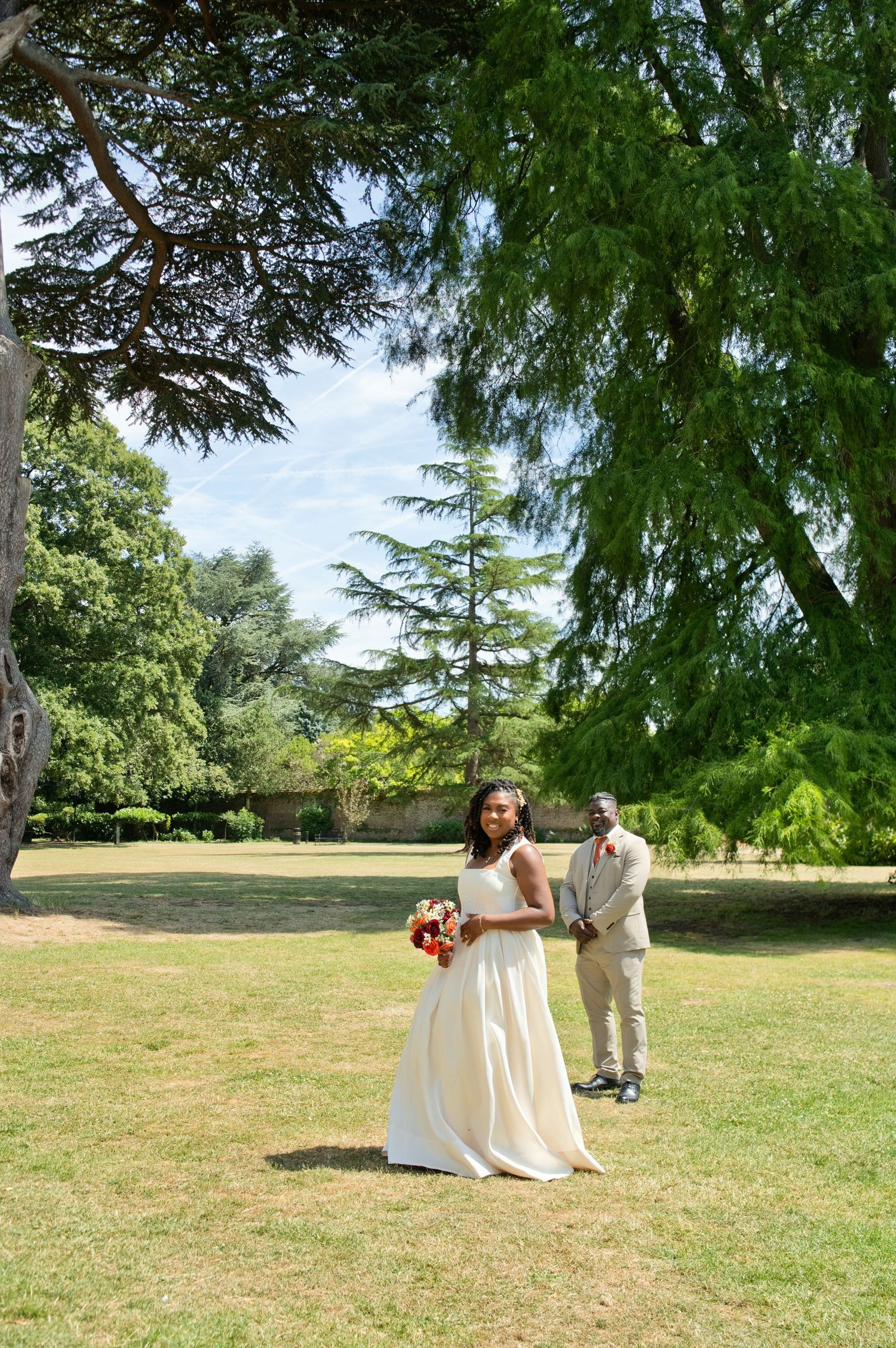 Alvanis and Bolu together in the park on their wedding day, framed by the trees.