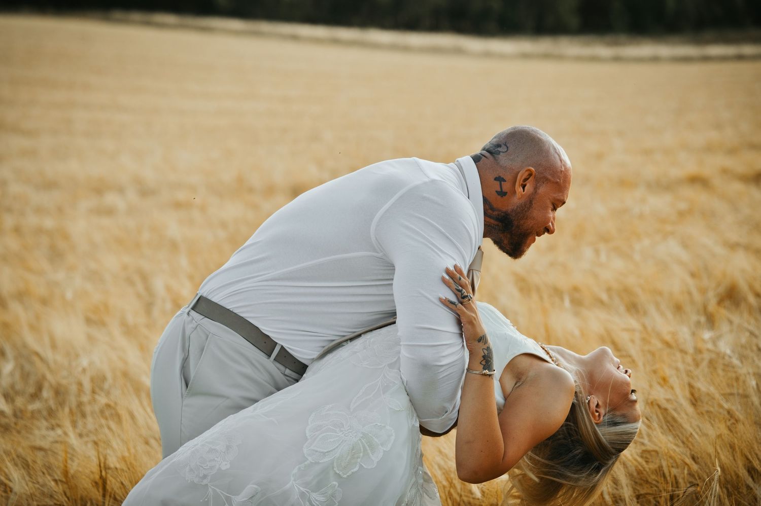 Tom dips Chloe back for a kiss in a golden field on their wedding day.