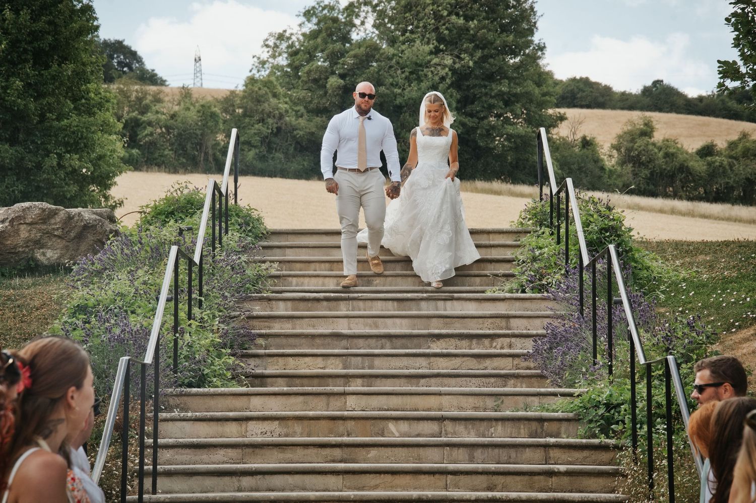 Chloe and Tom walking hand in hand down outdoor stone steps on their wedding day.