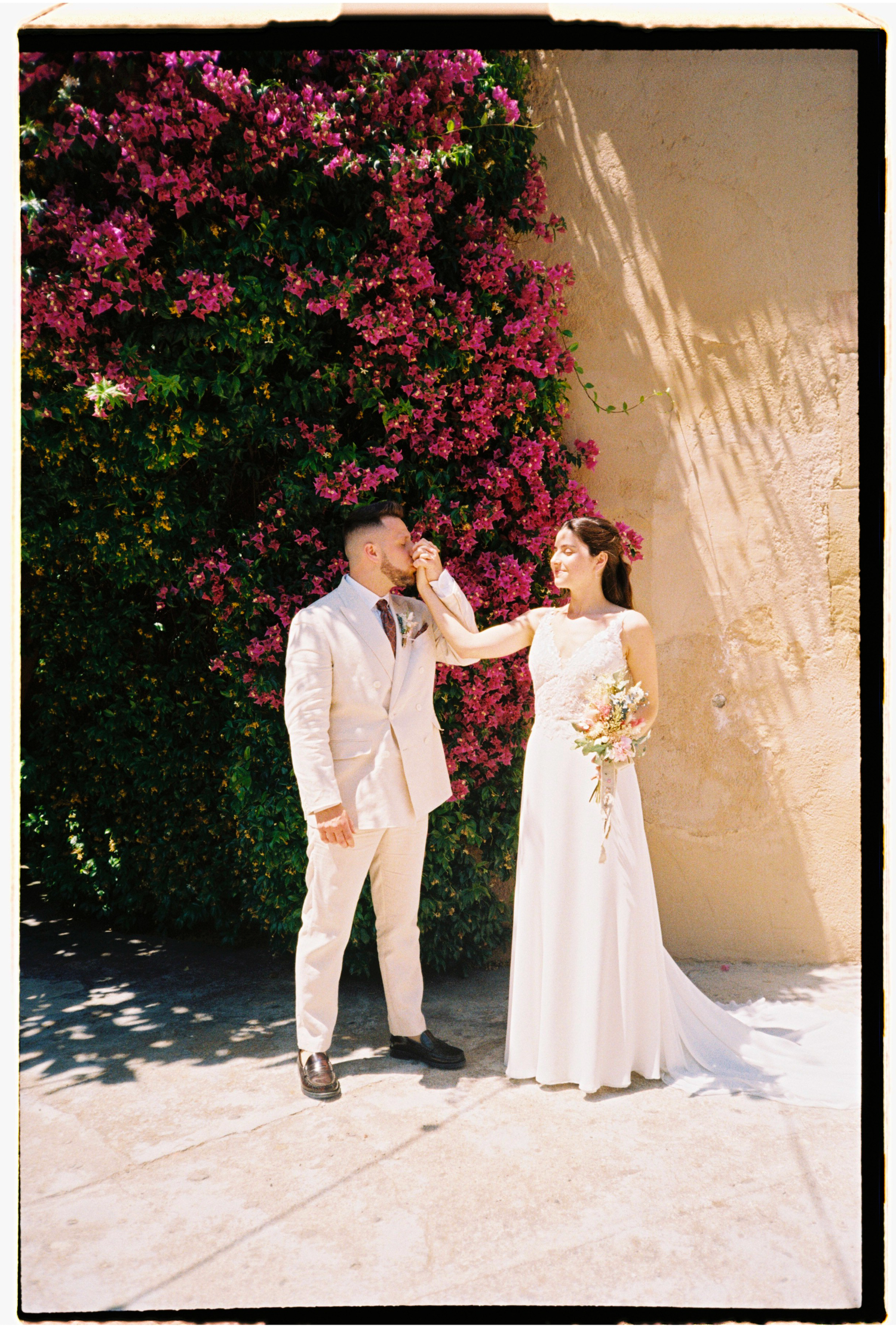 Bride and groom posing beneath vibrant bougainvillea during their summer wedding in Barcelona.