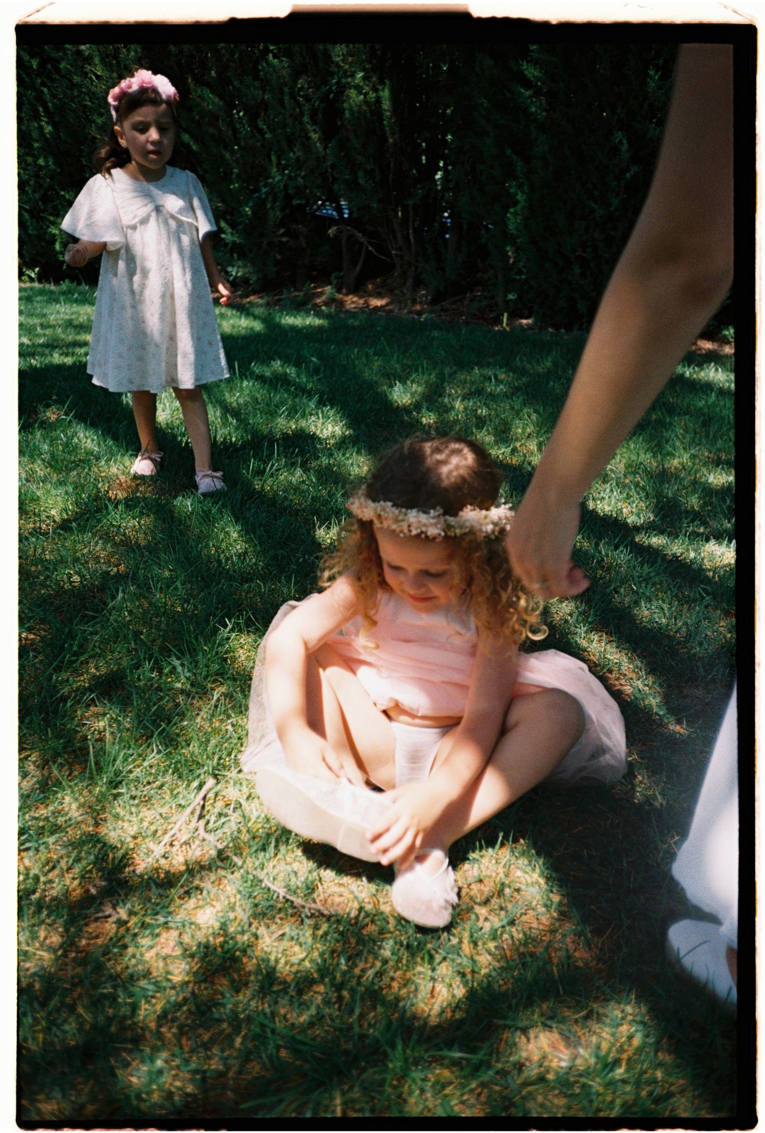Candid film photograph of a young wedding guest sitting in the shade during an outdoor celebration.