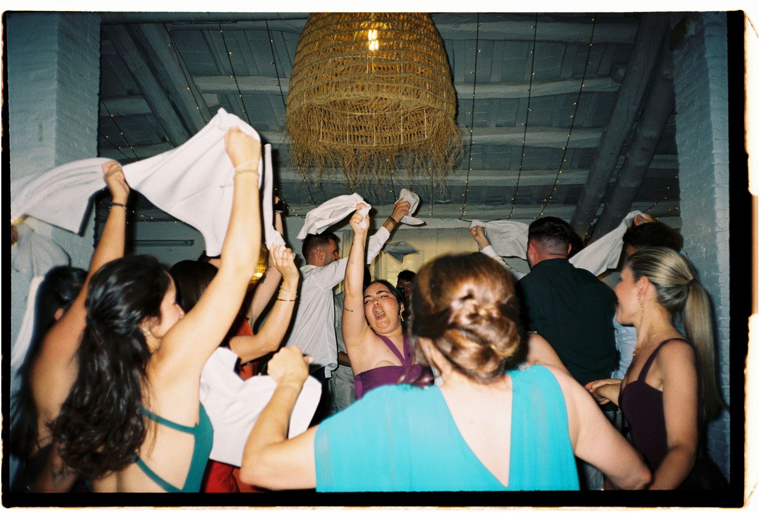 Candid film photograph of wedding guests dancing and celebrating during the reception.