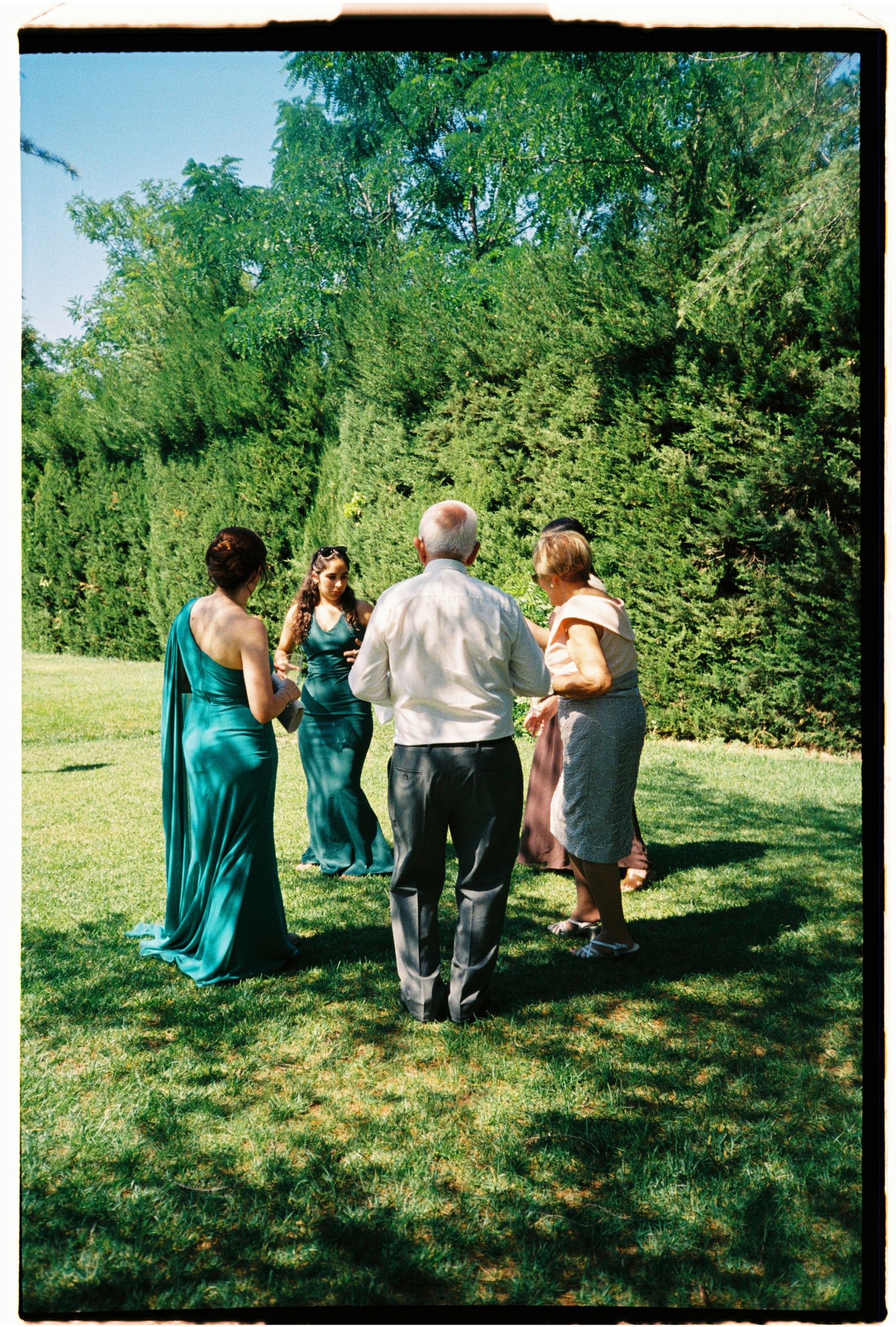 Candid film photograph of wedding guests walking through the garden during a summer celebration.
